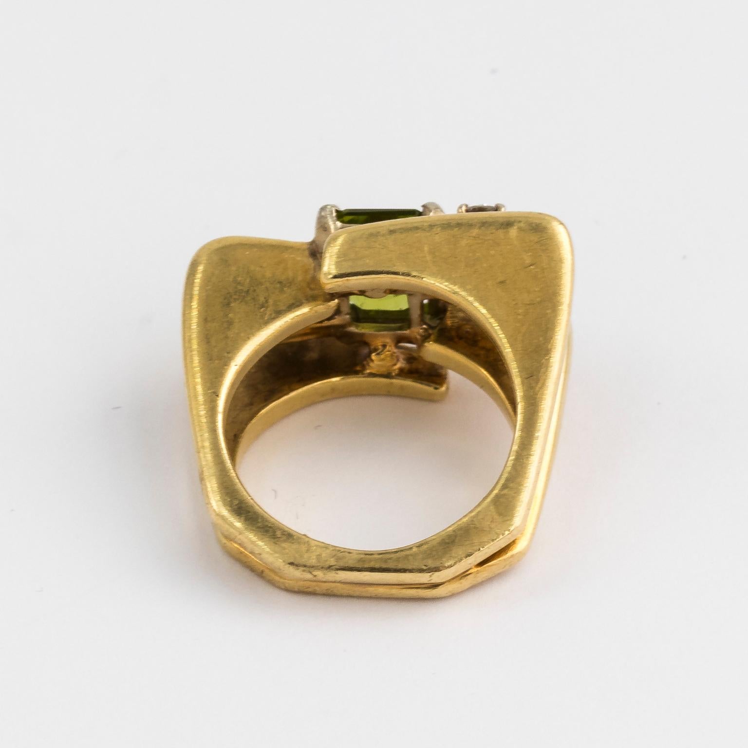 Circa 1970s 18 Karat Gold and Green Peridot ring with 0.50 carats of diamond. The center stone is green peridot flanked by two diamonds in a contemporary setting.
