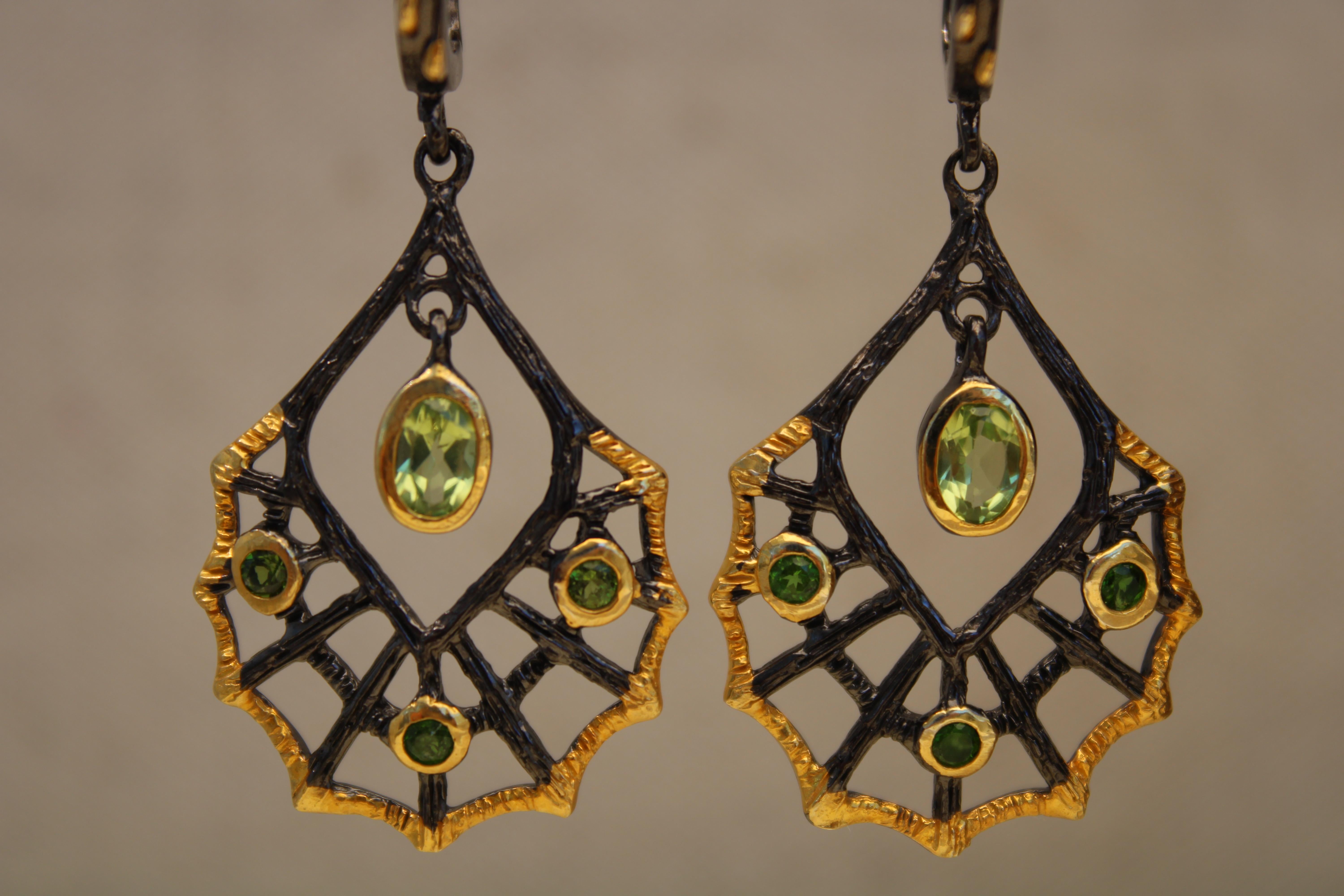 Pair of 14k gold plated and black rhodium dangle earrings set with 1 green peridot oval and 3 round green peridot stones on each side. These earrings feature a web design cast in black rhodium and gold plating over sterling silver. The oval peridot