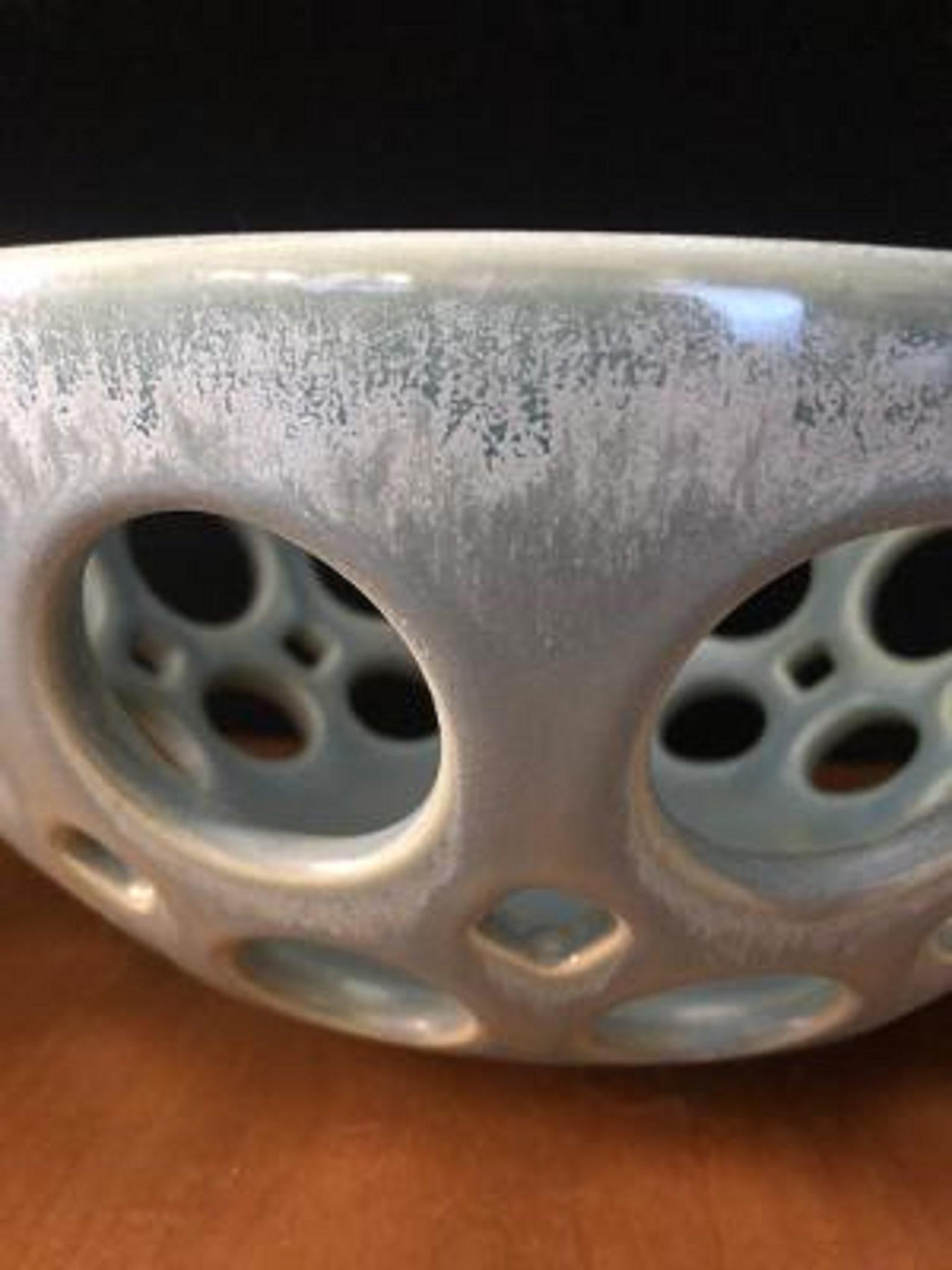 Inspired by Mid-Century Modern design, this bowl is wheel thrown and hand pierced stoneware. The satin glaze varies subtly from moss green to blue to gray. Controlled, slow cooling in the kiln allows tiny crystaline structures to form creating a