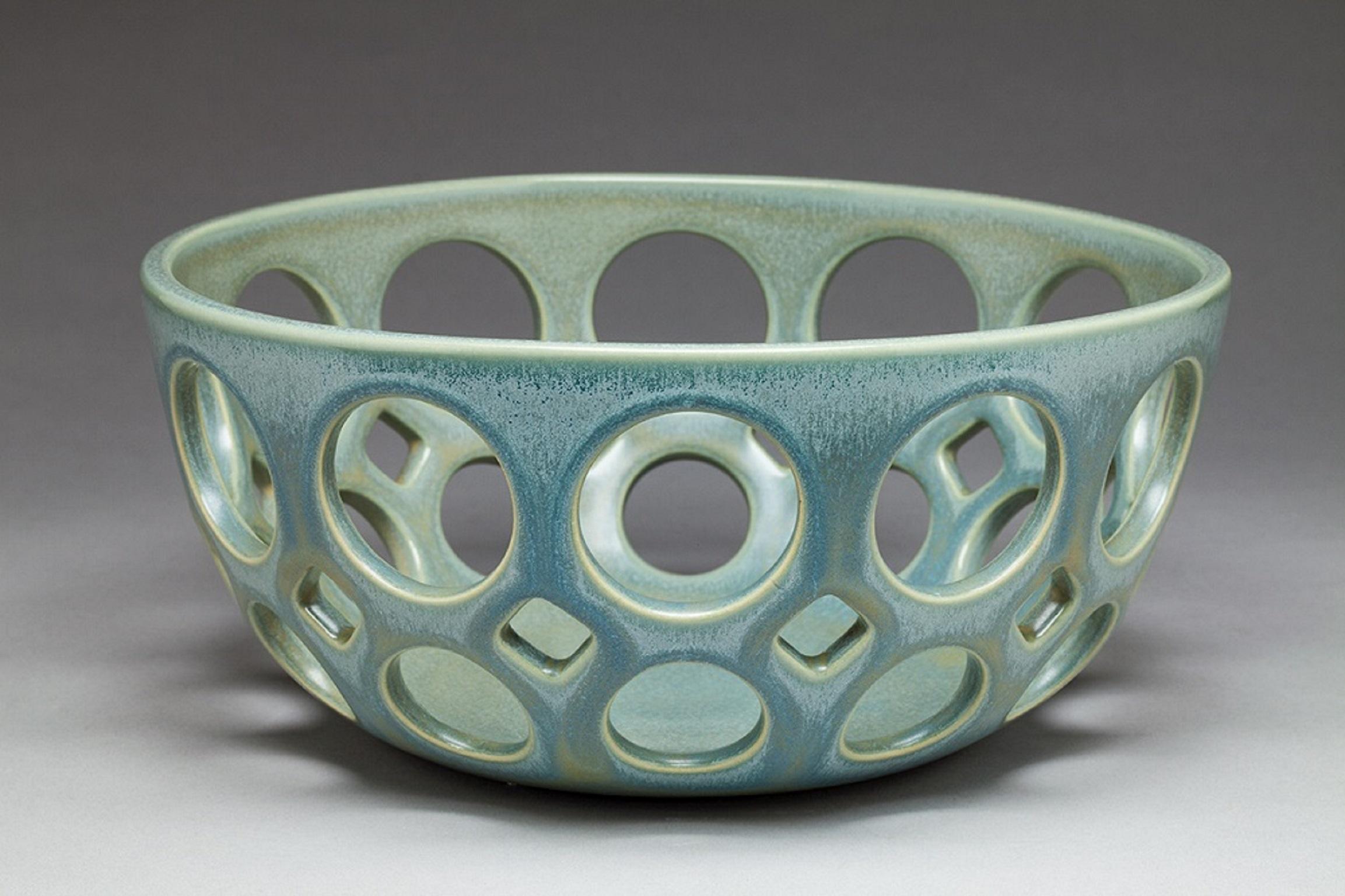 Inspired by Mid-Century Modern design, this bowl is wheel thrown and hand pierced stoneware. The satin glaze varies subtly from moss green to blue to gray. Controlled, slow cooling in the kiln allows tiny crystalline structures to form creating a