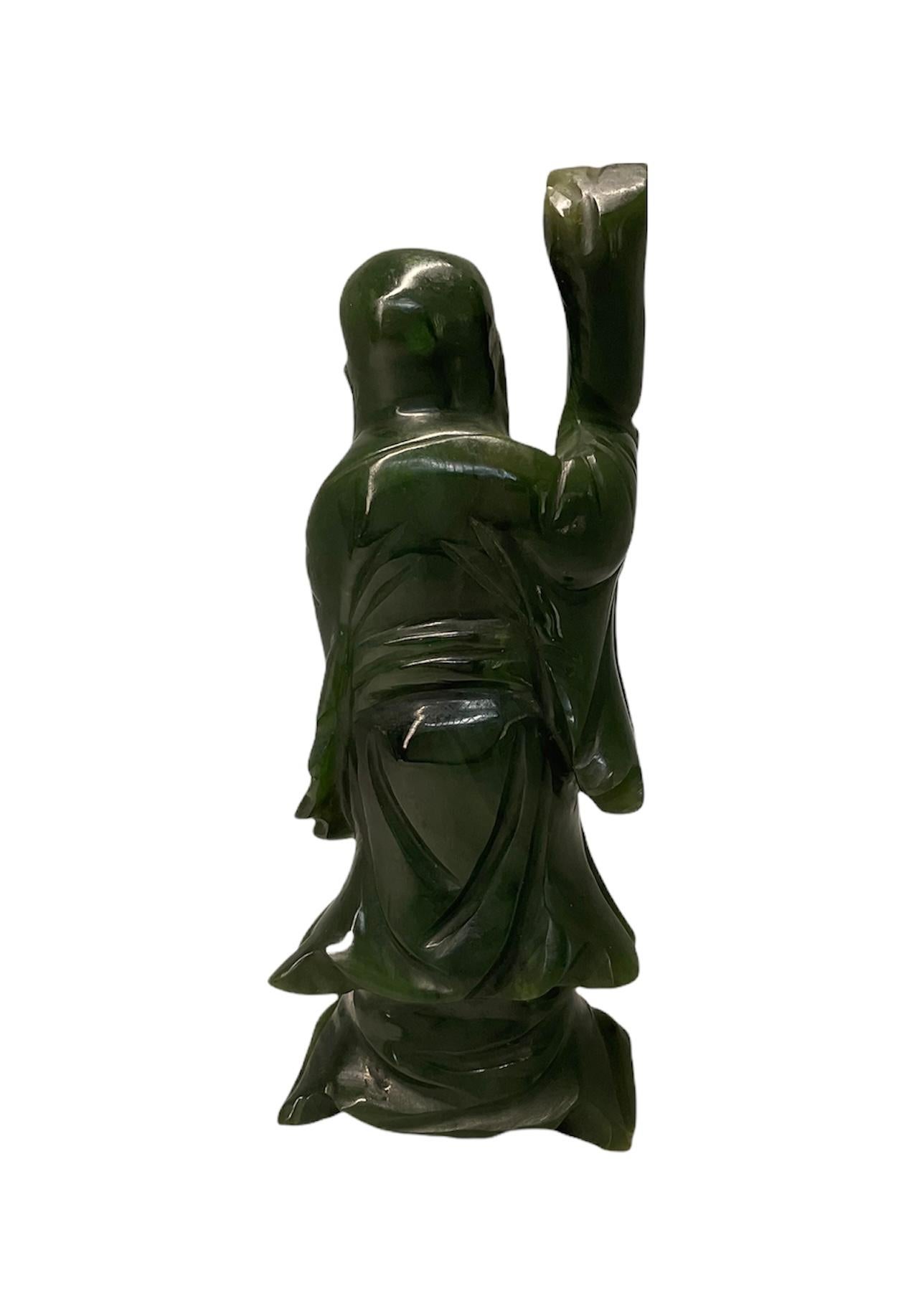 This is a hand carved green pine color jade small sculpture/figurine of Shou-Lao. It depicts an old man dressed with along robe. He has a very long beard and prominent bald head. He is holding a wood stick in his right hand and is holding a gourd