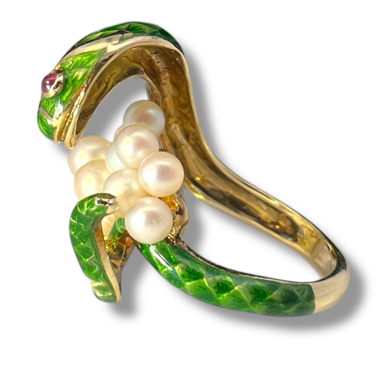 Questo anello in oro giallo 14k, testimonianza di maestria, riproduce l'ipnotica forma di un serpente arrotolato, il cui corpo è ornato da un vivace smalto verde che imita l'intricata struttura delle squame. I penetranti occhi di rubino del serpente