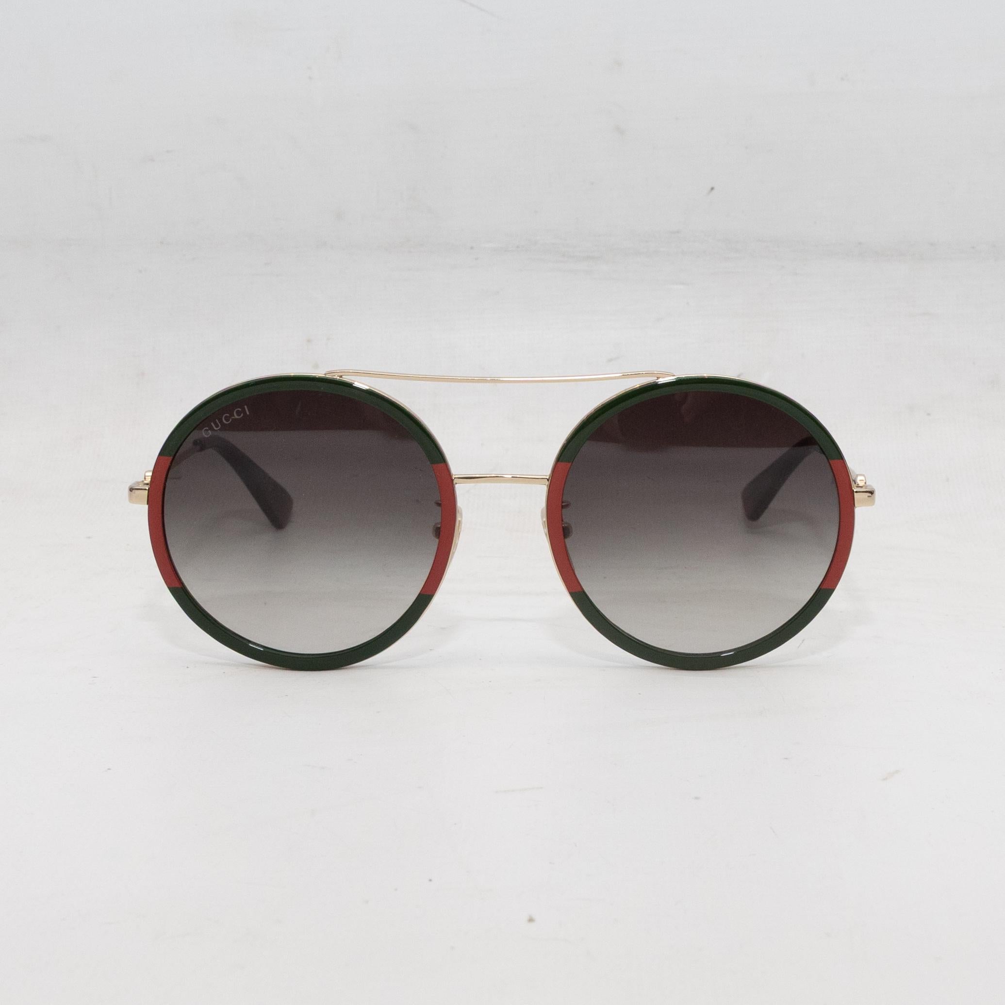 Green, red, and gold-tone round aviator sunglasses by Gucci. Adjustable nose pads. Grey tinted lenses. 2.25