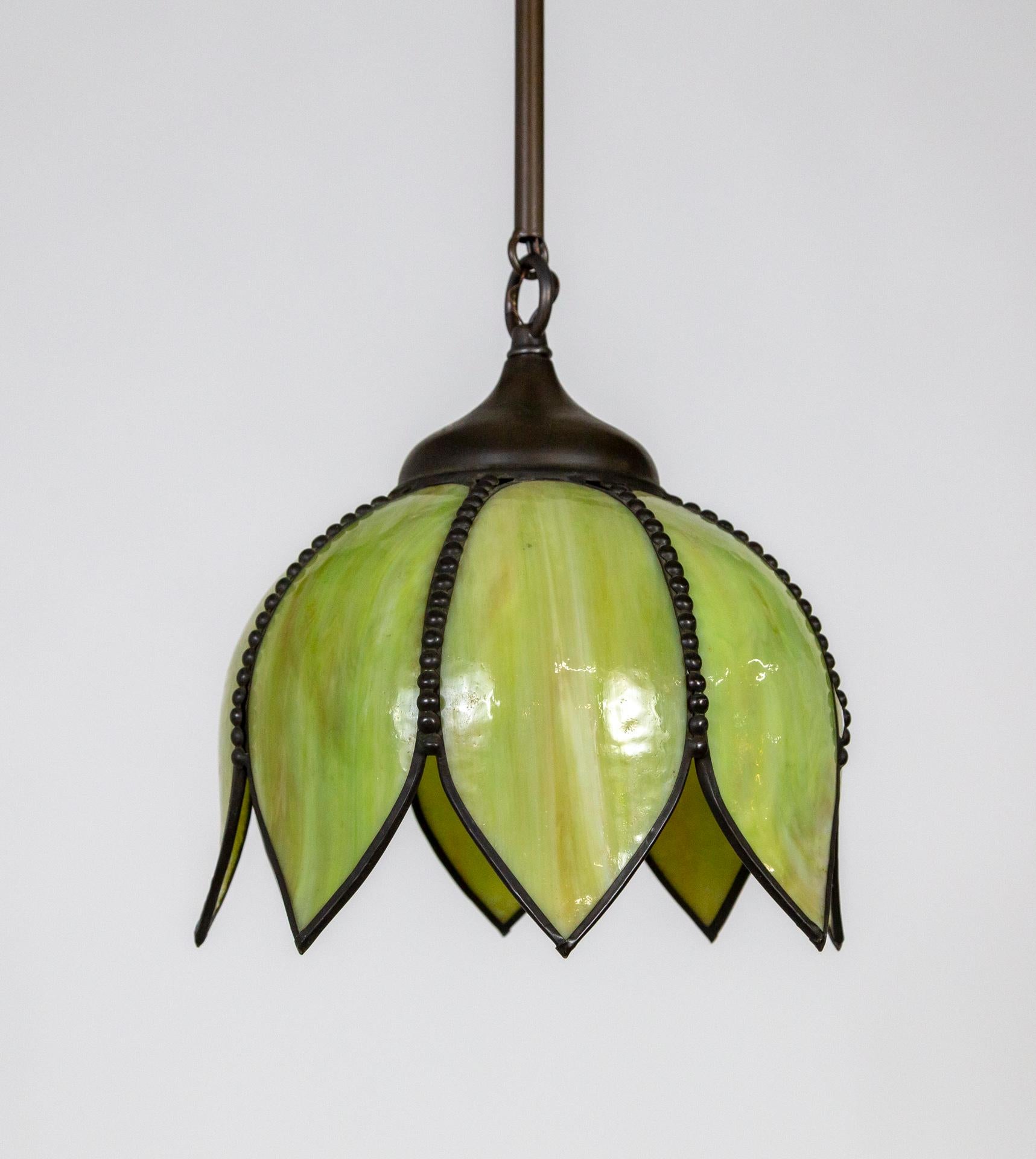 A mid century, green, slag glass, tulip-lotus pendant light. It changes to a yellow tone when lit. Each petal is lined with beaded brass. Newly wired with a segmented, linked stem in matching, darkened brass finish. We have two of these available.