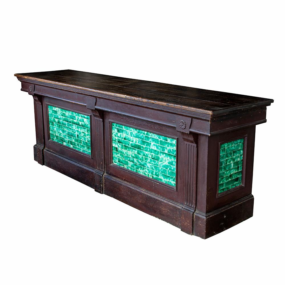 This unusual antique store counter has a beautiful depth of color with dark wood and mottled gem green and white tile. Some carved accents in the form of daisies and reeded pilasters add additional hints of detail to this lovely piece. The open back