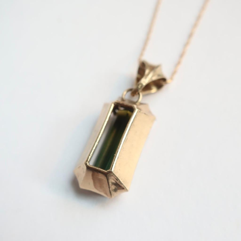 A statement necklace that mixes elegance, edge and sleek design- this solid 14K yellow gold pendant features the most stunning ombre green tourmaline baguette. The hand crafted bail hangs on an 18 inch white gold chain.  