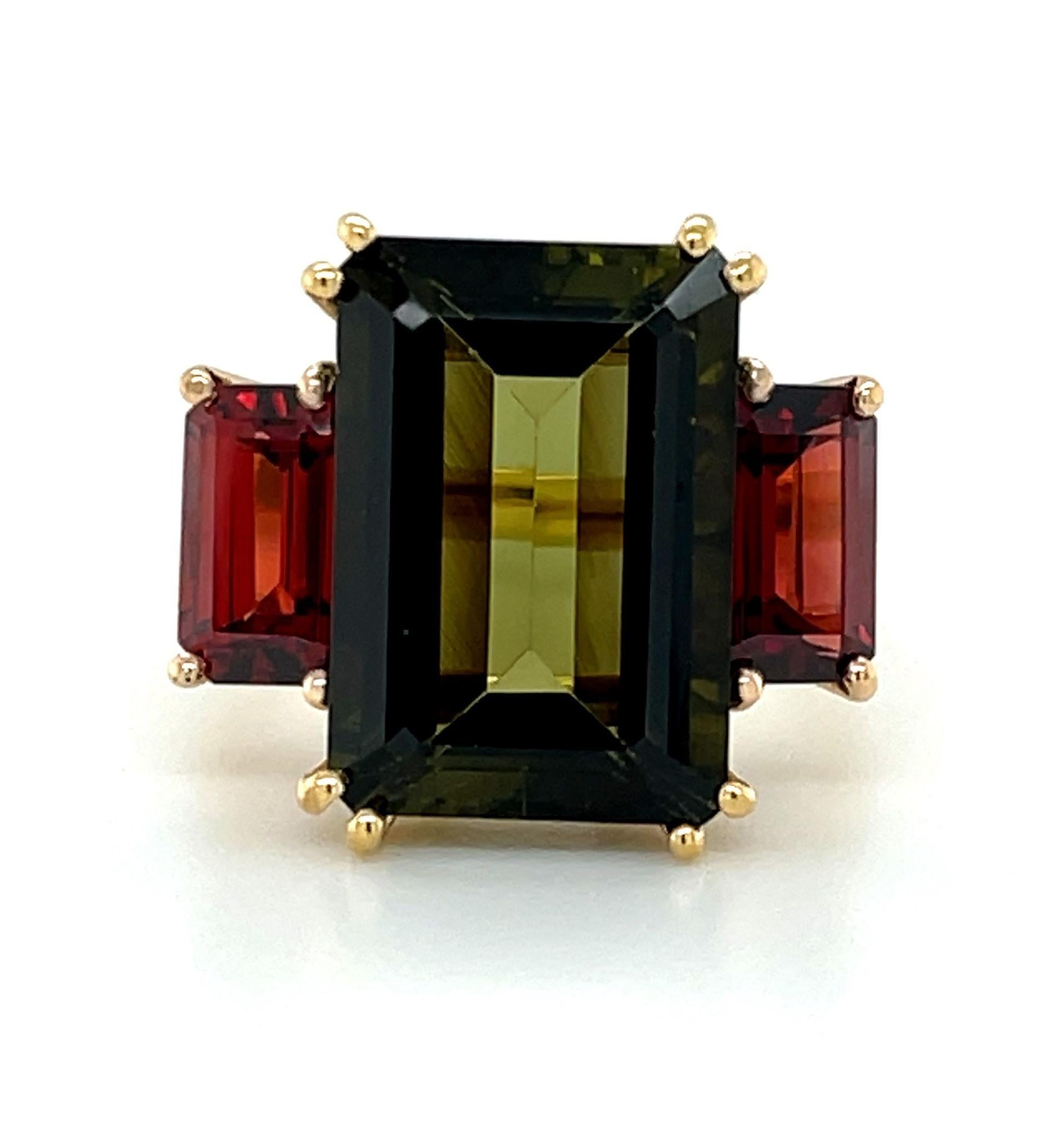 This unusual 3-stone cocktail ring features a large, 8.74 carat emerald-cut olive green tourmaline set with rich, red garnet side stones set in 18k yellow and rose gold. The center tourmaline is a crystalline gem with earthy, olive green color,
