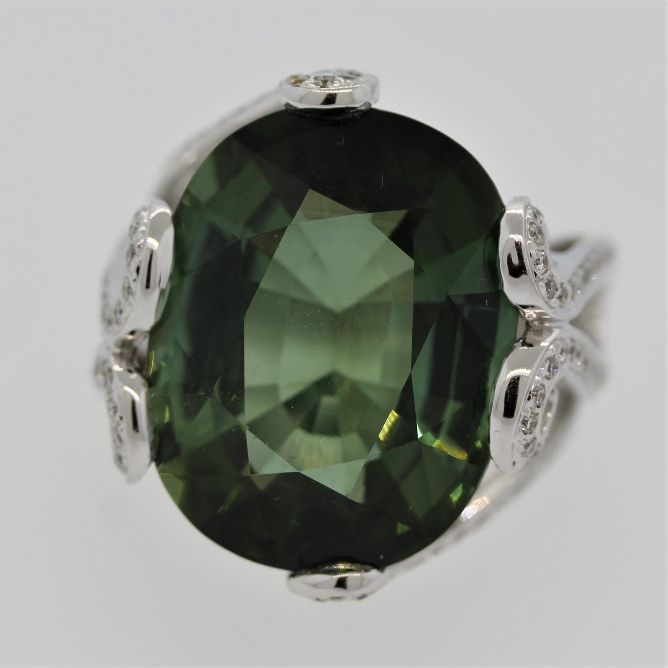 A beautiful 22.95 carat green tourmaline is featured in an 18k white gold ring. It is cut as a lovely oval and has a clean green color with a hint of blue with no visible inclusions. It is accented by 0.60 carats of round brilliant cut diamonds