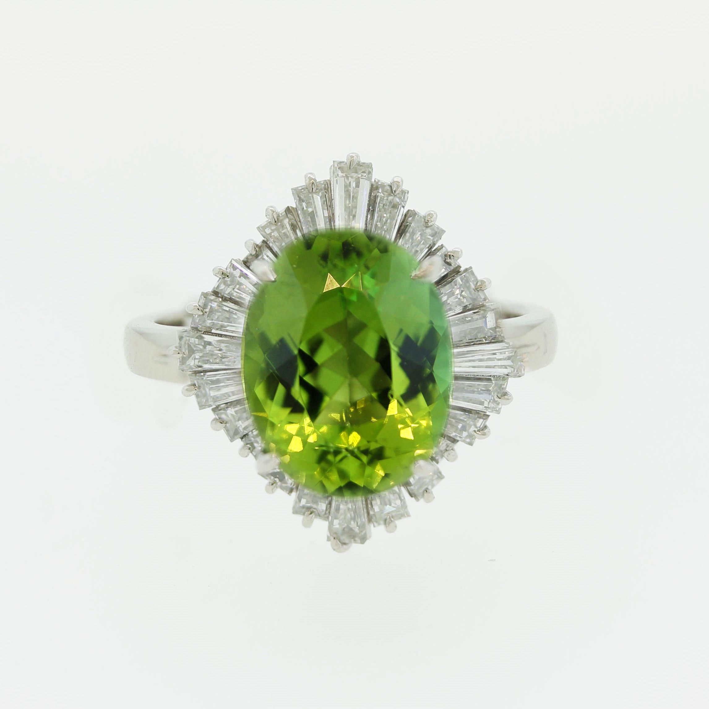 A vibrant and vivid green colored tourmaline weighing 4.10 carats takes center stage. It has a lovely oval-shape and is accented by 1.48 carats of baguette-cut diamonds set around it in a ballerina style. Hand-fabricated in platinum and ready to be