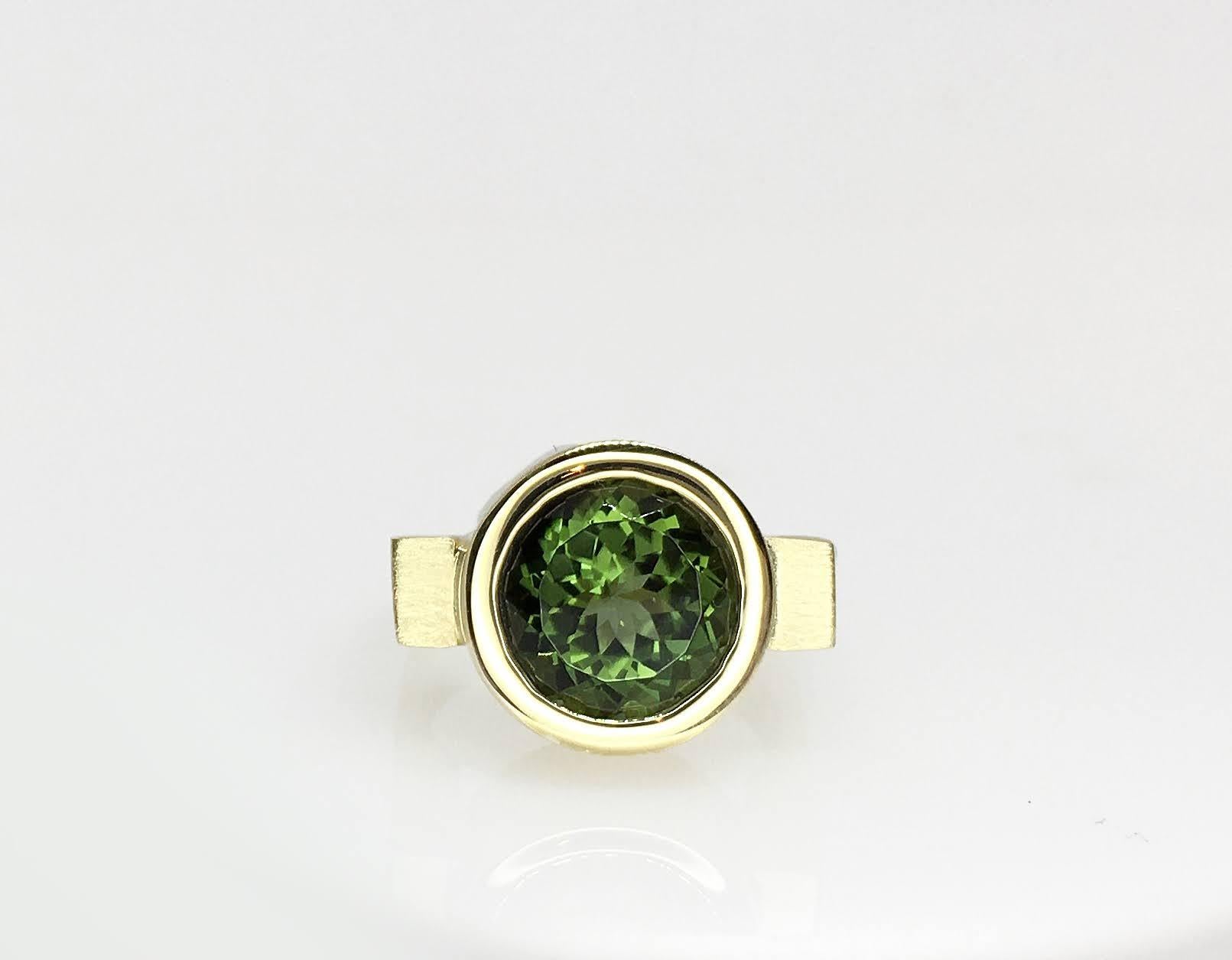 This Green Tourmaline Bezel Ring is shown here in yellow gold. A round bezel set on a squared band with a high polish finish creates an infinitely modern look. Be careful, this ring will bring you much attention, if that’s what you’re aiming for,