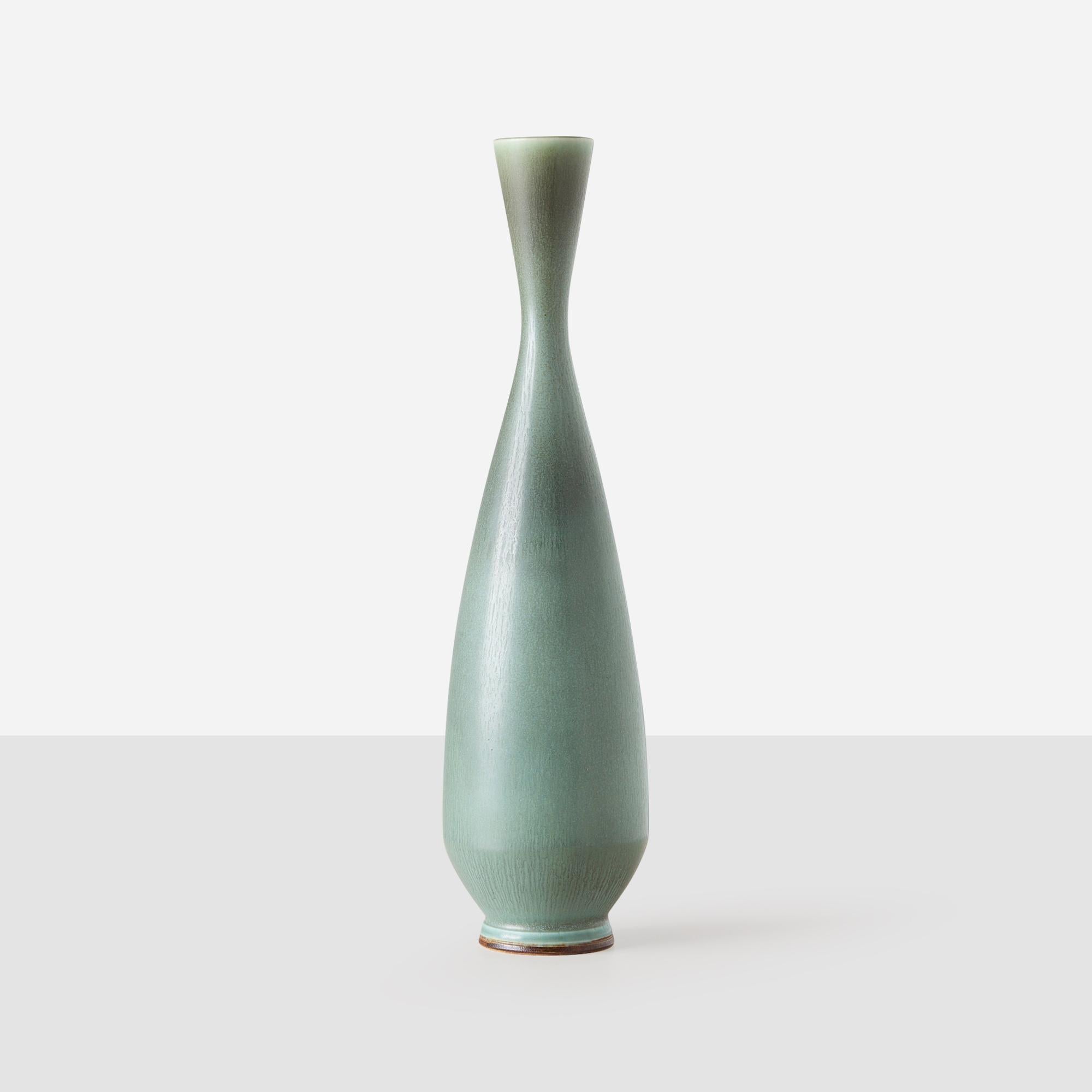 This wheel-thrown stoneware vase by Berndt Friberg features a long, thin neck and a smooth glaze in hues of pale greens and greys. It exemplifies Friberg’s refined craftsmanship and elegant form. The underside is etched with “Friberg” and marked