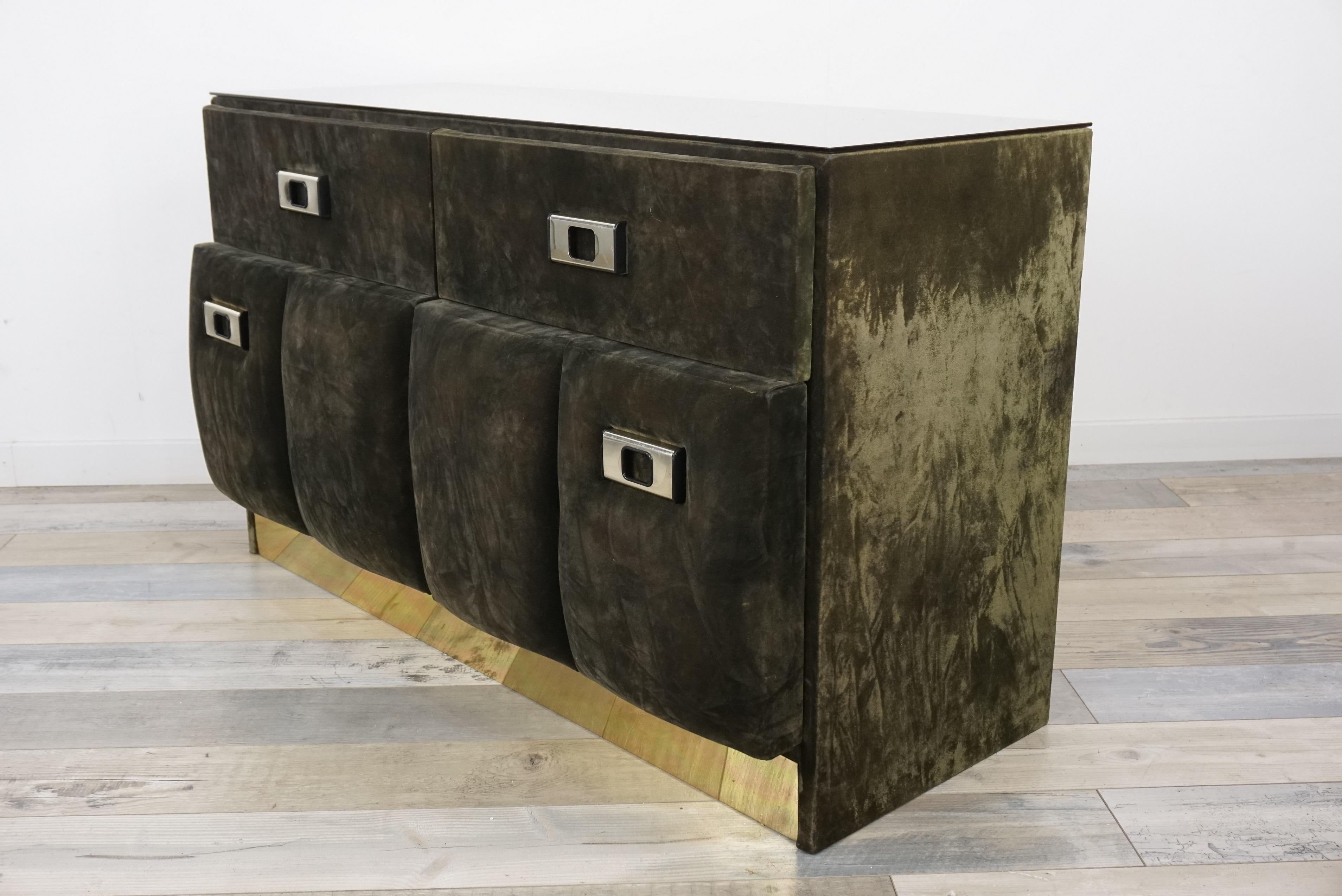 This green forest velvet dresser with generous and plump shapes, with an Italian design from the 1960s and 1970s, is adorned with a mirror-effect glass top tinged with bronze and a brass finish on the front for the base. It is composed of handles, 2