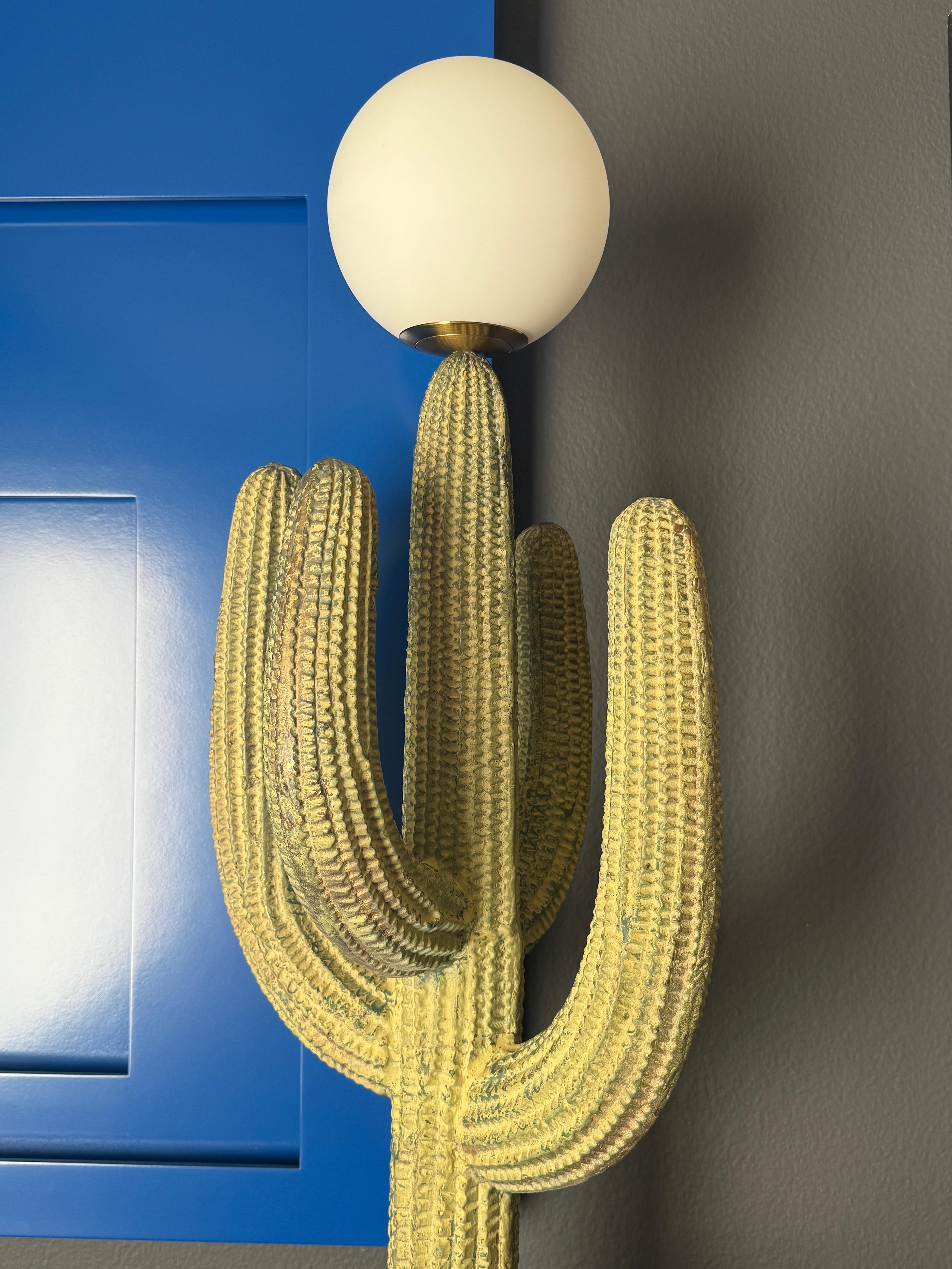 Lámpara escultura de cactus saguaro de latón patinado en verdigris verde con correcaminos montada sobre una base de madera negra. El globo tiene un diámetro de 15 cm y requiere una bombilla LED con base de candelabro de hasta 60 vatios.