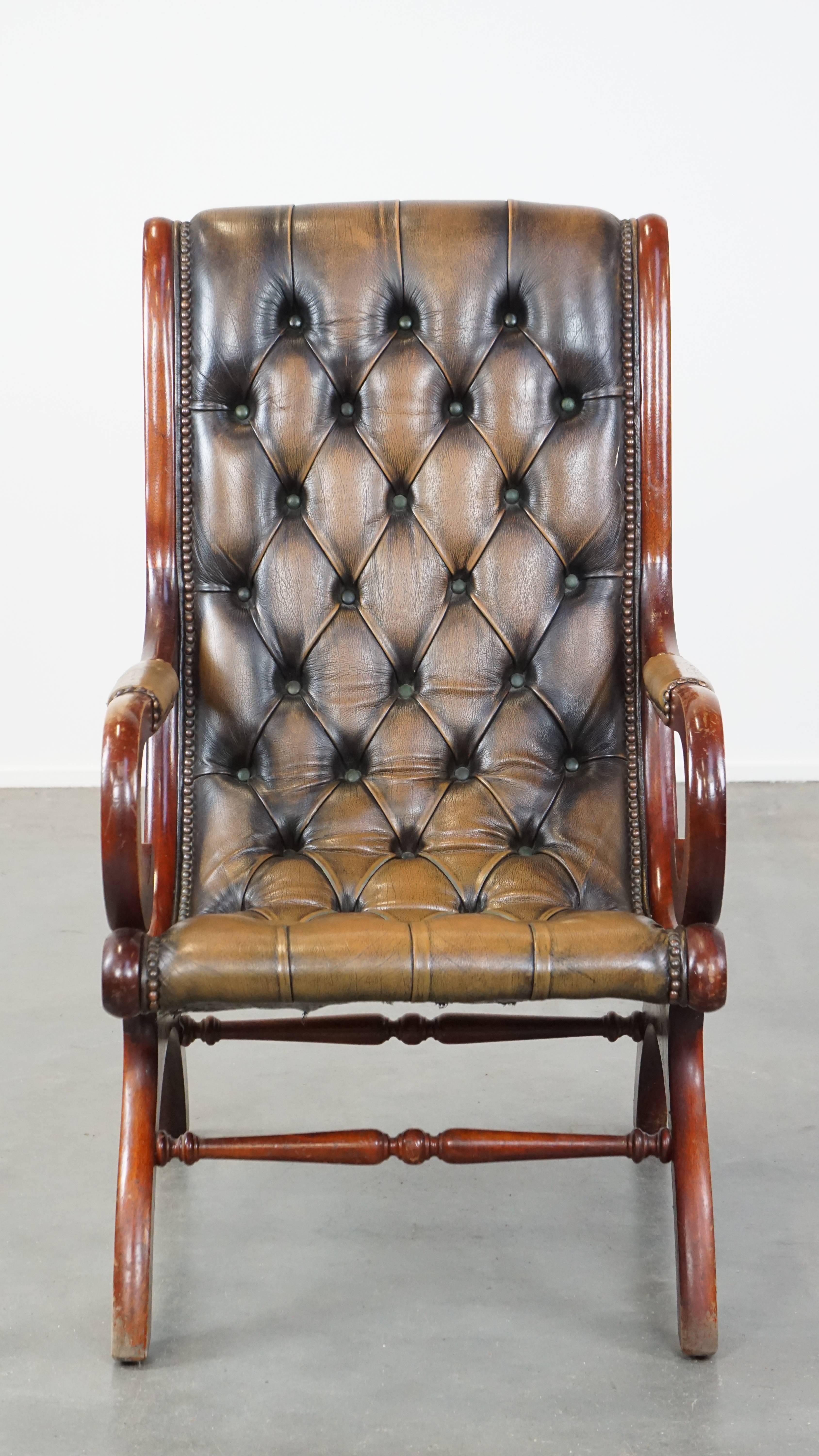 This vintage leather Chesterfield armchair exudes the beloved timeless English class and style. It features a graceful design, a bold green color scheme, and is neatly finished with decorative nails. The chair is combined with wood and offers