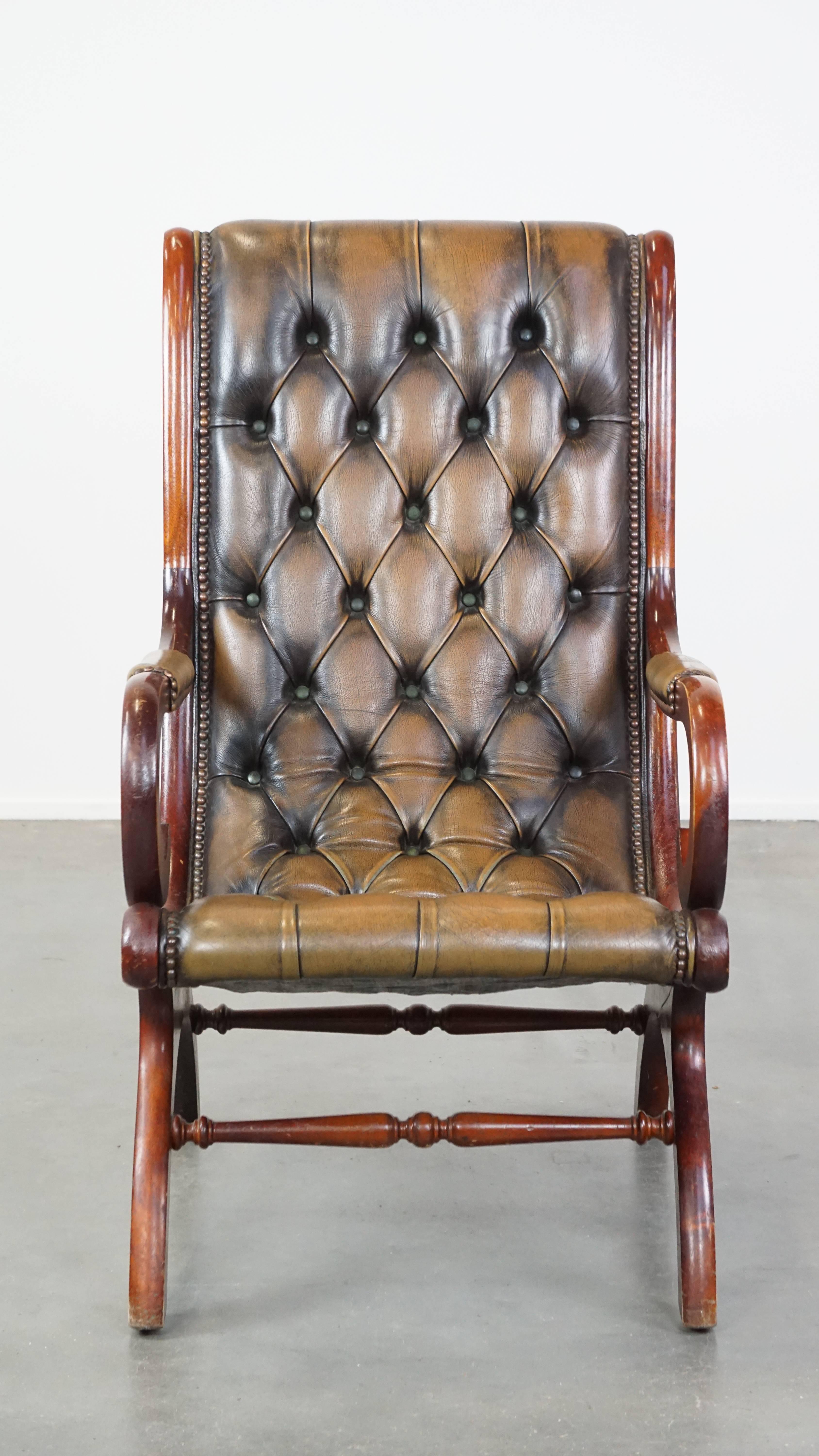 This vintage full-grain leather Chesterfield armchair exudes the beloved timeless English class and style. It features an elegant design, a bold green color scheme, and is beautifully finished with decorative nails. Combined with wood, this armchair