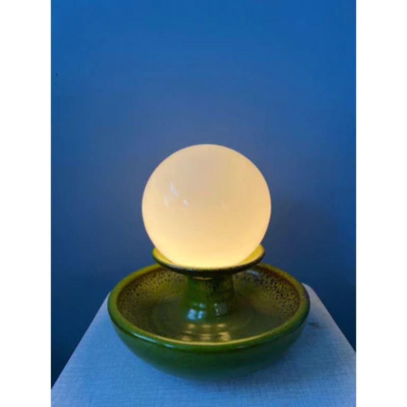 A green west germany vase and table lamp with a glass shade. The shade lies loose on the vase. The green ceramic bowl rests on two small legs and a small hand grip on the other end. The lamp requires one E14 lightbulb and currently has an