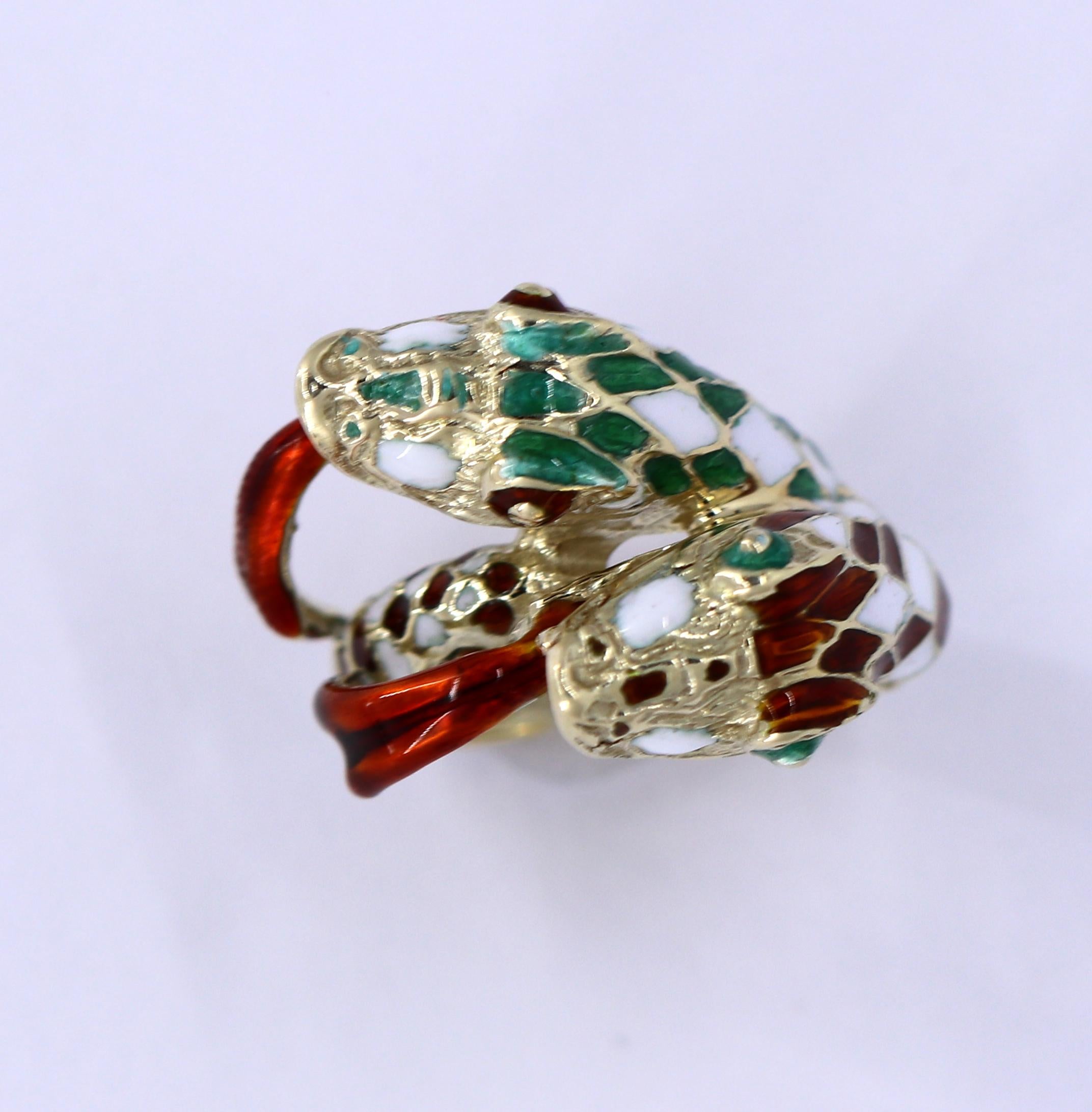An 18K yellow gold ring centered around a double headed, mythical snake. With multi-colored enameled scales, the colorful serpent features burgundy/red, green, and white. Tapering in width from 1/4 inches wide at the base up to 5/8 of an inch at the
