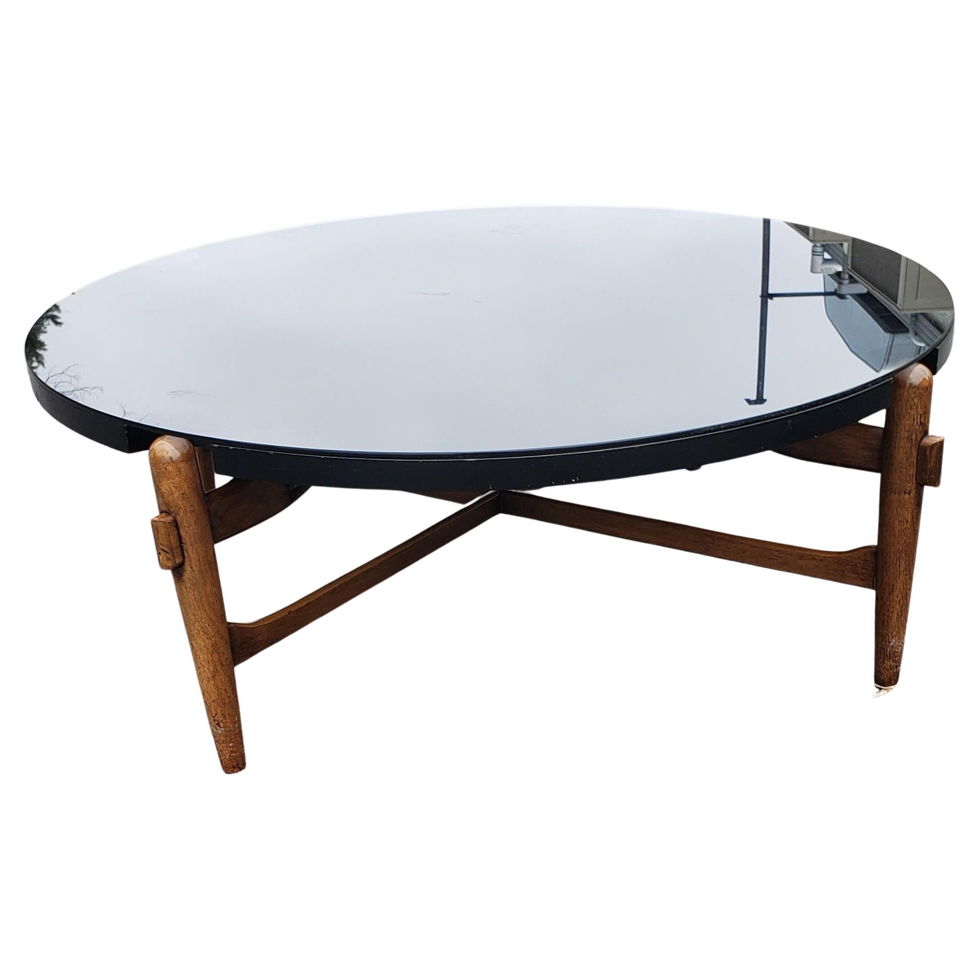 A 1950s Greta Grossman designed Danish modern coffee table featuring a round black laminate top with notches to allow for the four leg posts, sculptural wood frame with cross-stretchers, original finish. Protective smoked glass top in very good