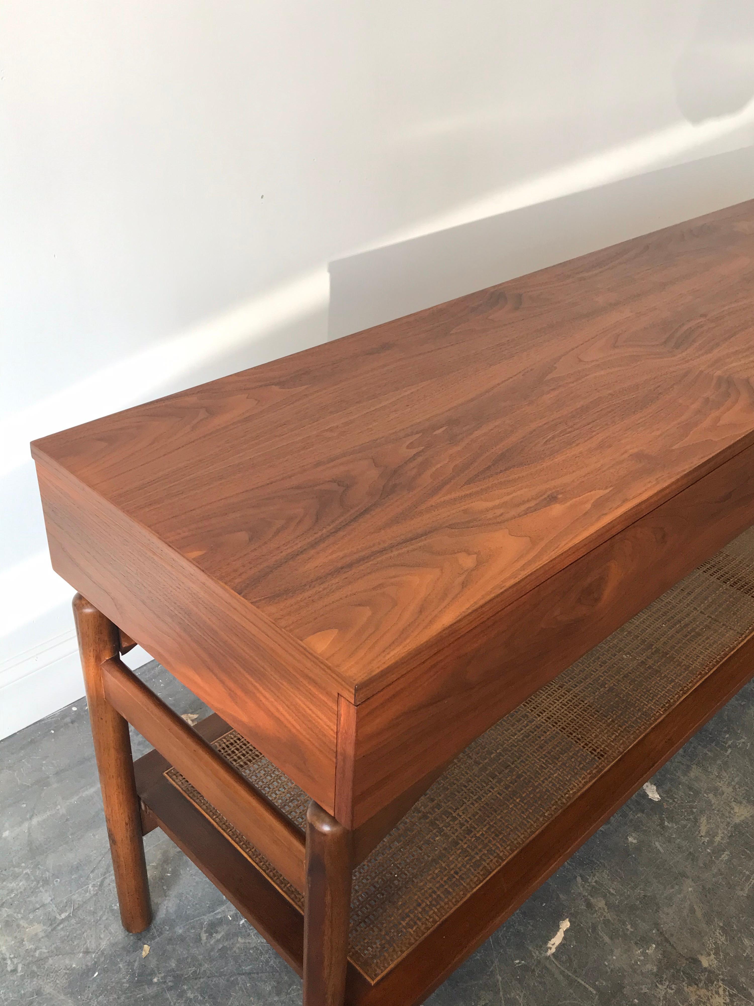 A stunning walnut console table designed by Greta Grossman for Glenn of California. Console features a three drawer case floating above a cane shelf. Drawer on the right is felt lined. Top, sides, and drawer fronts all refinished. Legs have been