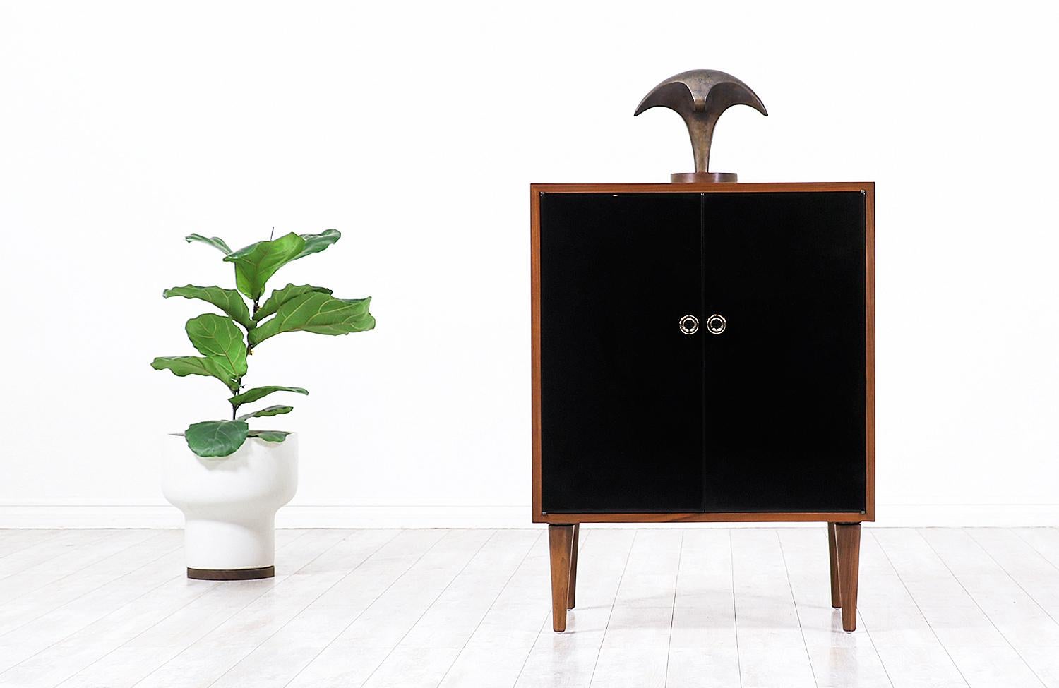 An elegant lacquered cabinet designed by Swedish architect Greta M. Grossman for Glenn of California in the United States, circa 1950s. This two-door cabinet features a solid walnut wood case with a glossy black lacquered finish on the doors, and