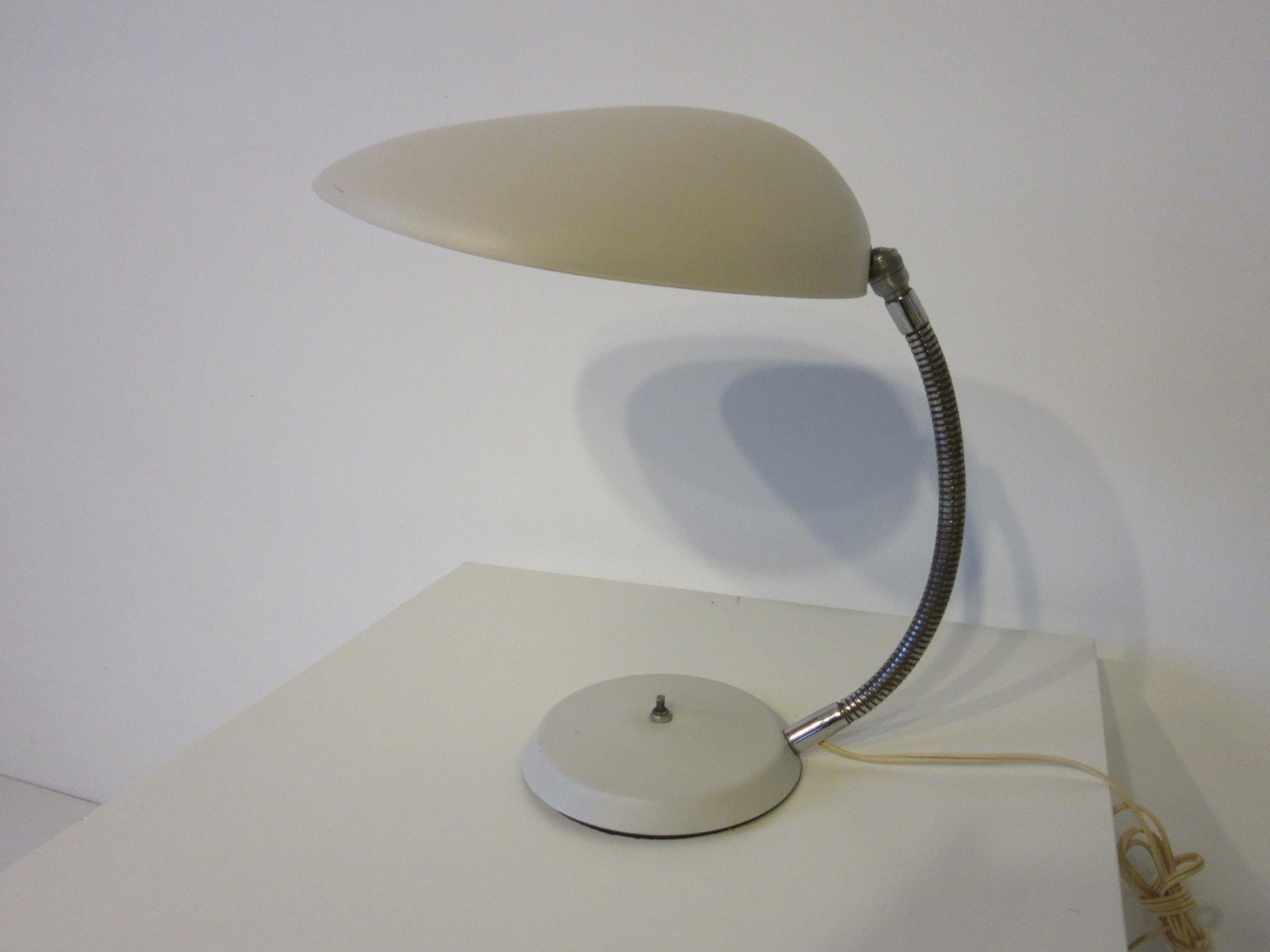 A iconic midcentury cobra table lamp in a satin off white finish on the metal shade and base with push button switch and flexible satin chrome arm. Manufactured by the Ralph O. Smith Modern Lighting Company model number 901 - T from designer Greta