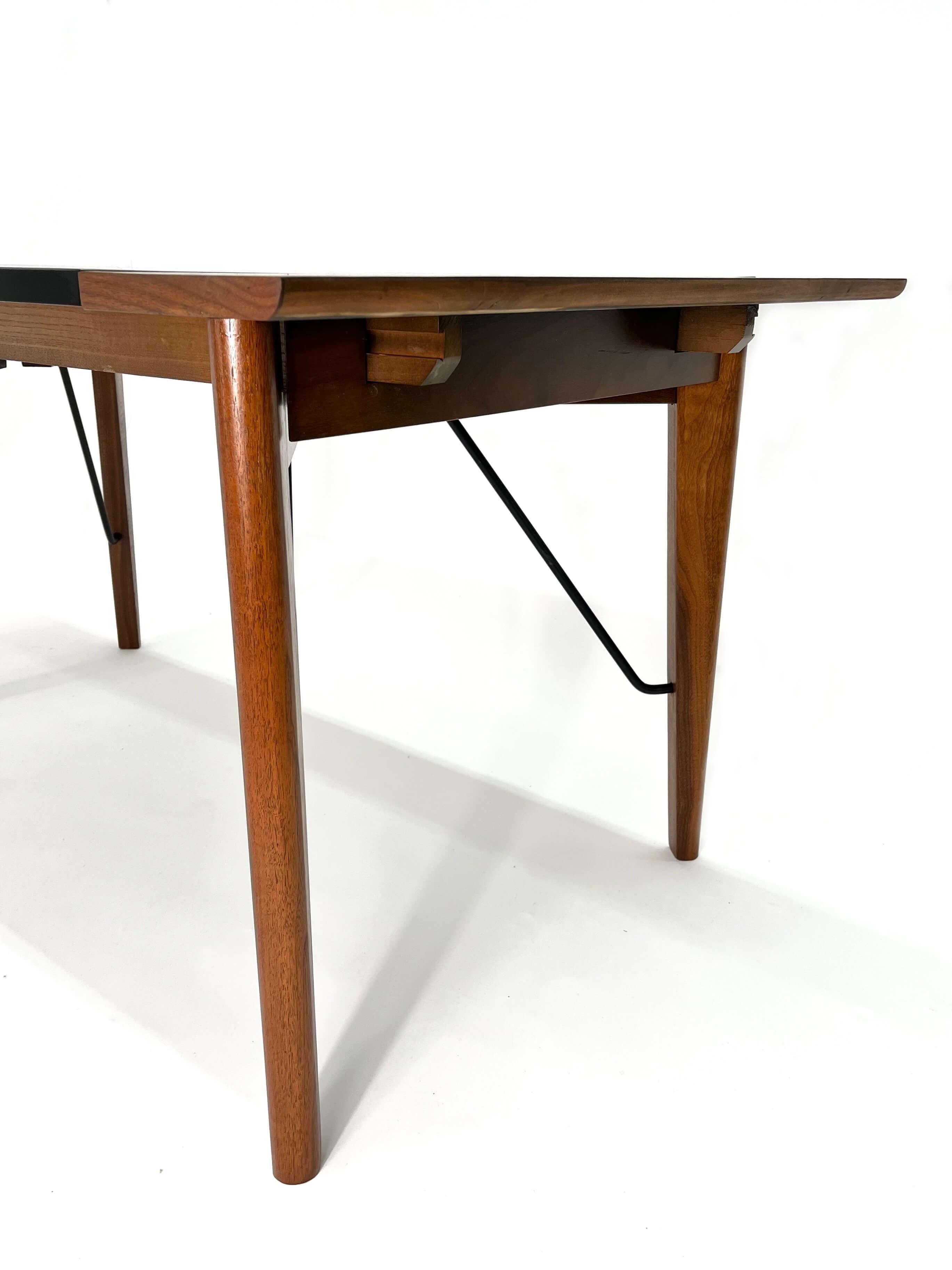 Rare Rectangular dining table by Greta M. Grossman for Glenn of California, circa. 1950s. The table features a solid walnut wood frame with a black laminate top and iron stretchers supporting the legs. The expandable table has two removable leaves,