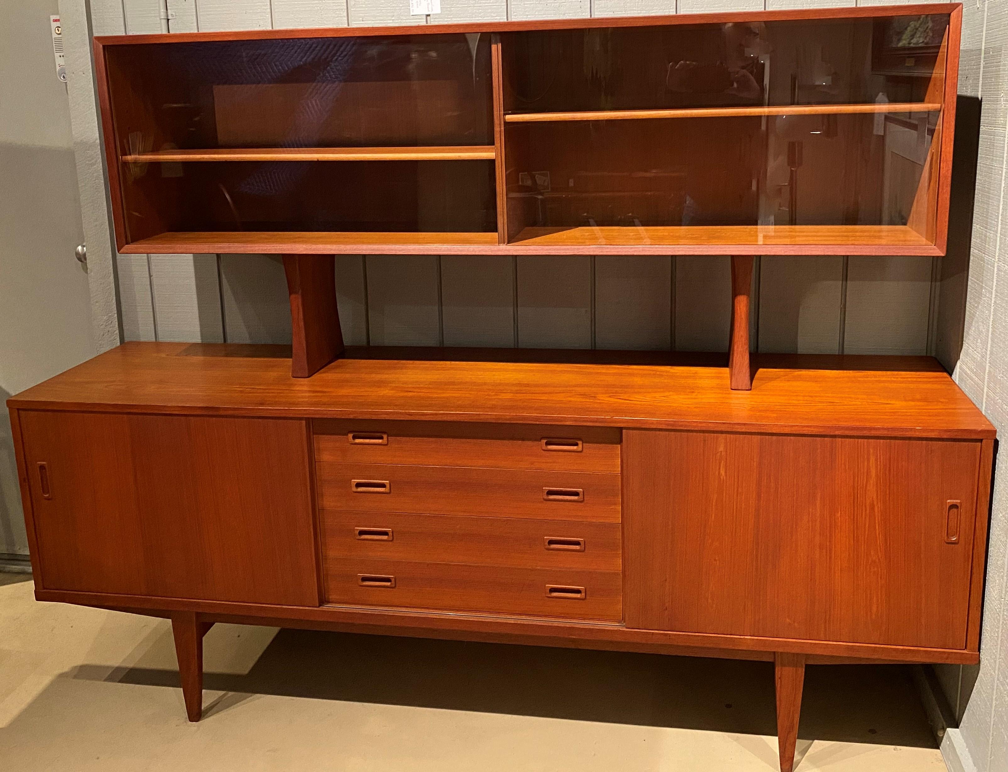 A sleek design midcentury teak credenza by Danish designer Grete Jalk (1920-2006) with a removable upper display cabinet with two sliding glass doors opening to two adjustable single shelf compartments, over a lower case with an inset set of four