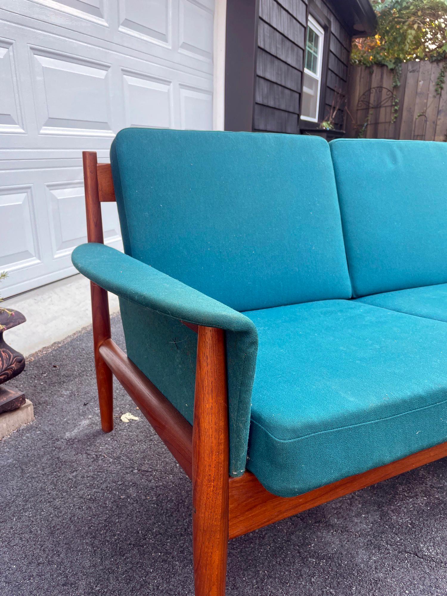 A stunning four seat teal textile upholstered sofa designed by Grete Jalk for France and Sons of Denmark. Frame is made of teak. The cushions are spring loaded. Original France and Sons badge is intact on the frame. In excellent condition with