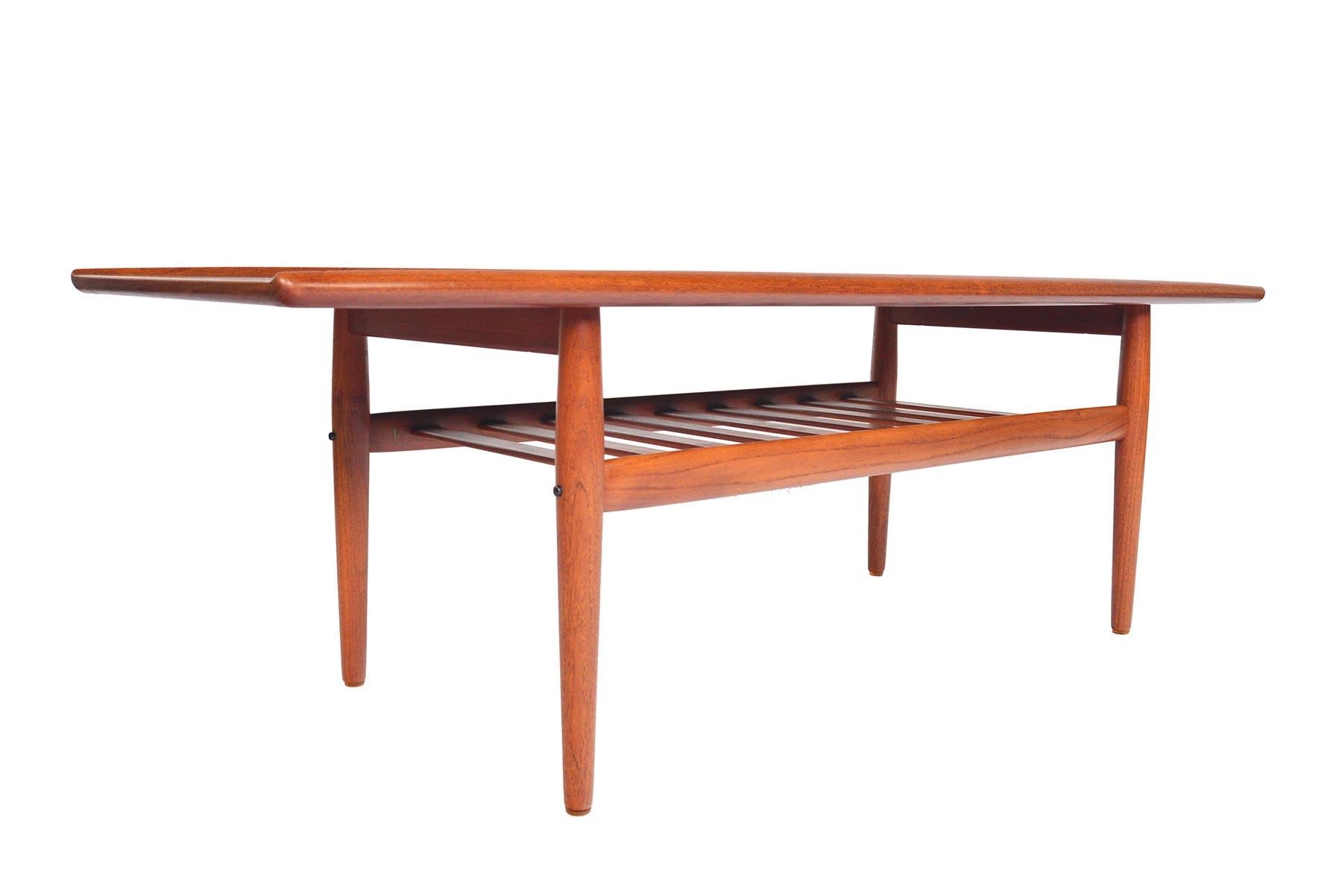 This elegant Danish modern midcentury surfboard coffee table was designed by Grete Jalk for Glostrup Mobelfabrik in the 1960s. Beautiful book- match veneer is flanked by raised lips. A lower rack offers storage. In excellent original condition.

 