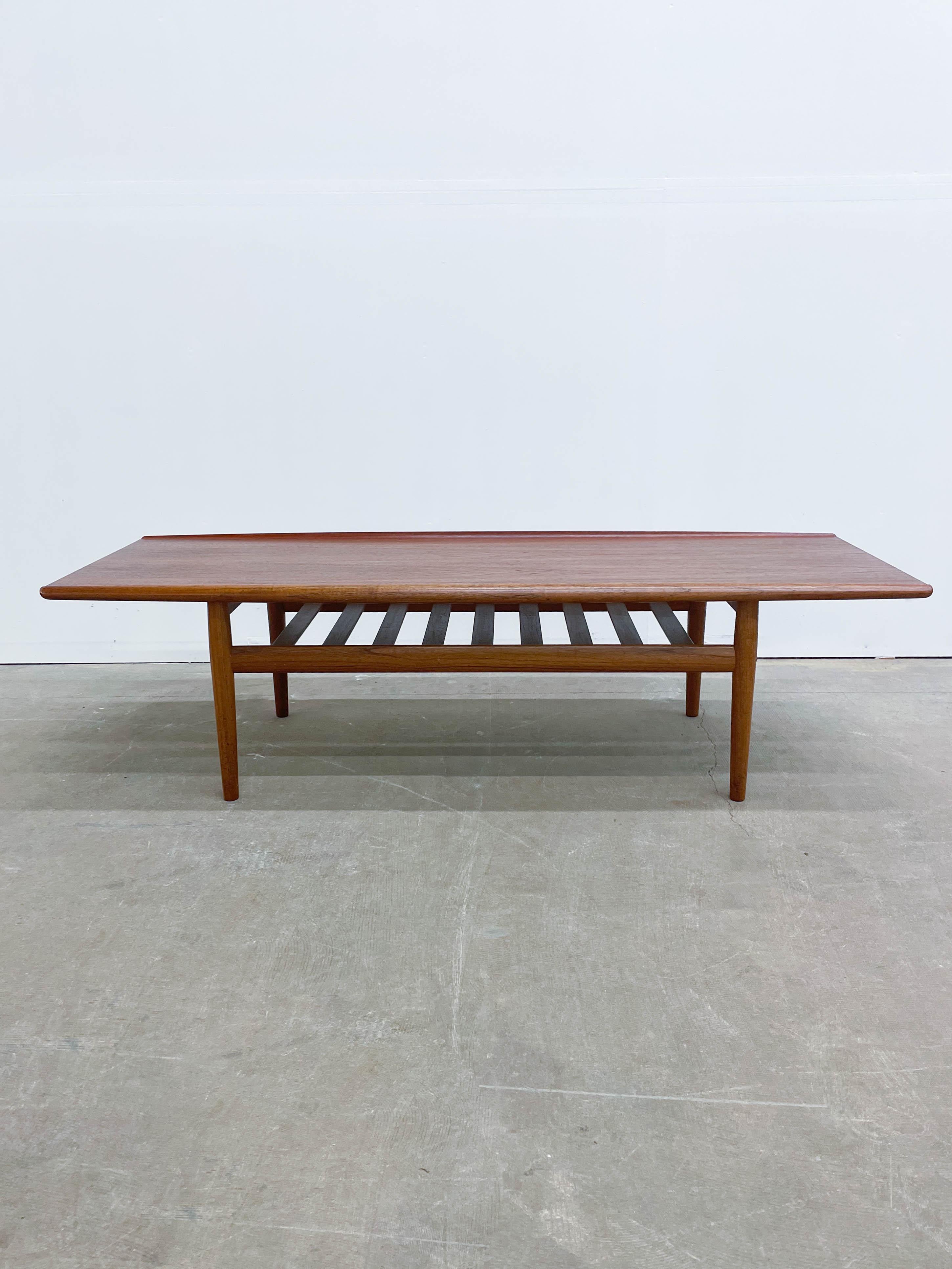 This beautiful Danish Modern Teak coffee table was designed by the iconic Grete Jalk and dates back from the 1960s. Made by Poul Jeppessen in Denmark, this table features an expansive top with rolled edges, superb teak woodgrain, a functional