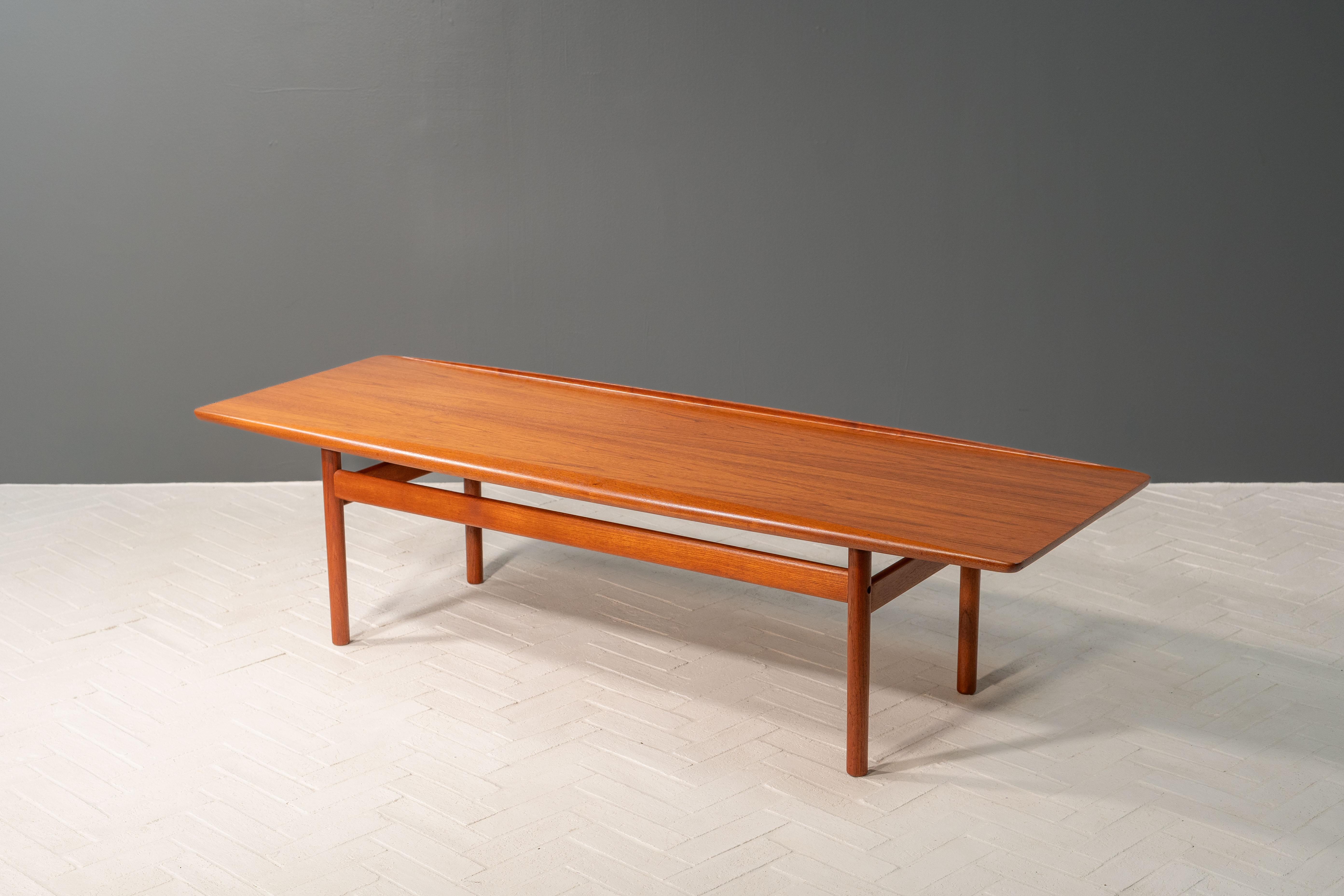 Danemark, vers les années 1960. Une table basse ou de cocktail longue et attrayante, créée par Grete Jalk pour Poul Jeppesen. Construction en teck avec plateau de planche de surf supporté par des pieds cylindriques avec des extensions parallèles