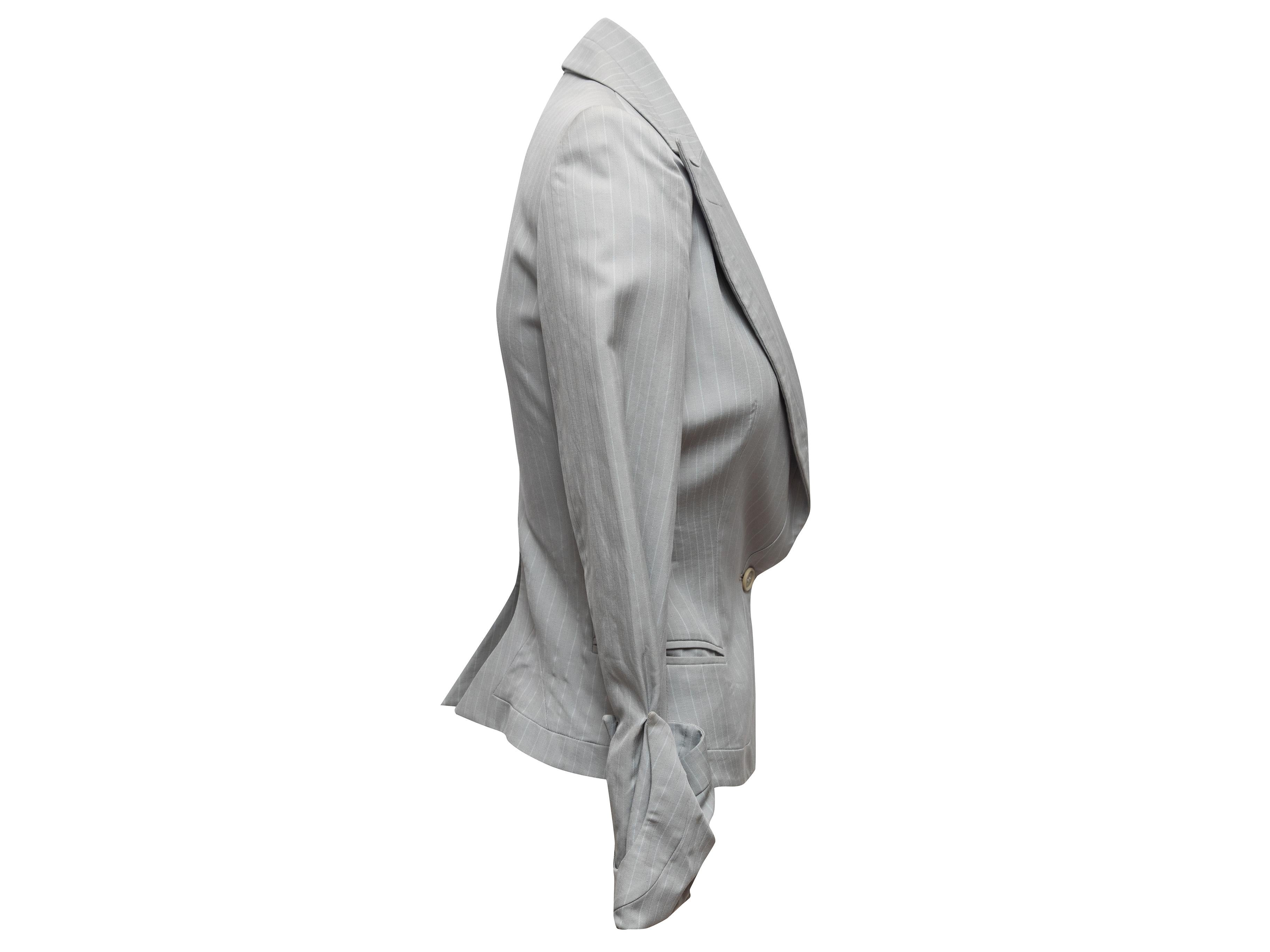 Gonna gessata grigia in lana e misto seta di Alexander McQueen. Il blazer è caratterizzato da rever a lancia, doppie tasche a filetto sui fianchi e chiusura con bottoni singoli sul davanti. La gonna presenta due tasche sui fianchi e una chiusura