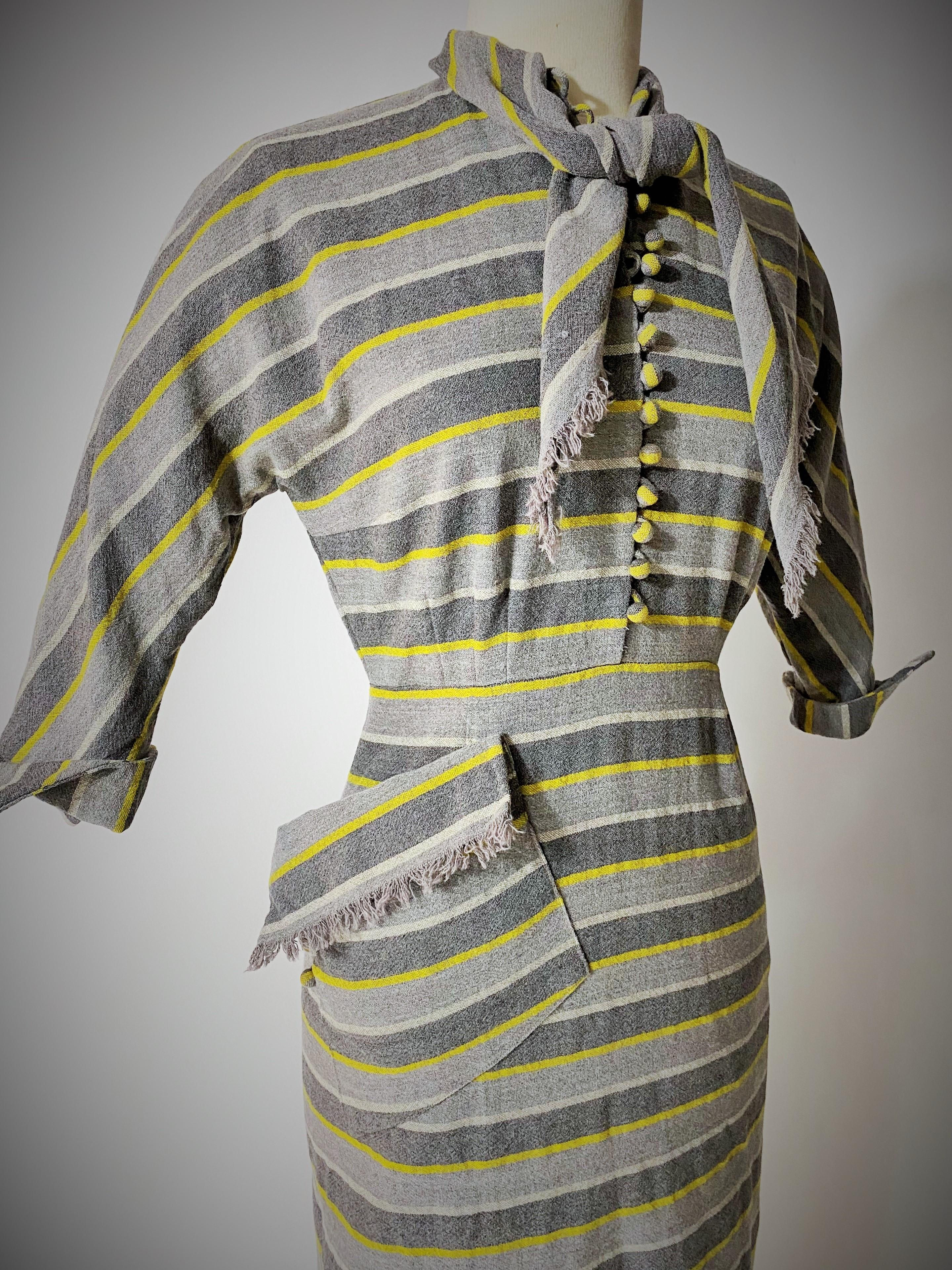 Circa 1945-1950
France
An early day dress in grey and yellow striped woven woolen cloth dating from the end of the Second World War.  Tight-fitting dress with darts and slits at the back, Kimono sleeve cut, closed at the front by bell buttons with