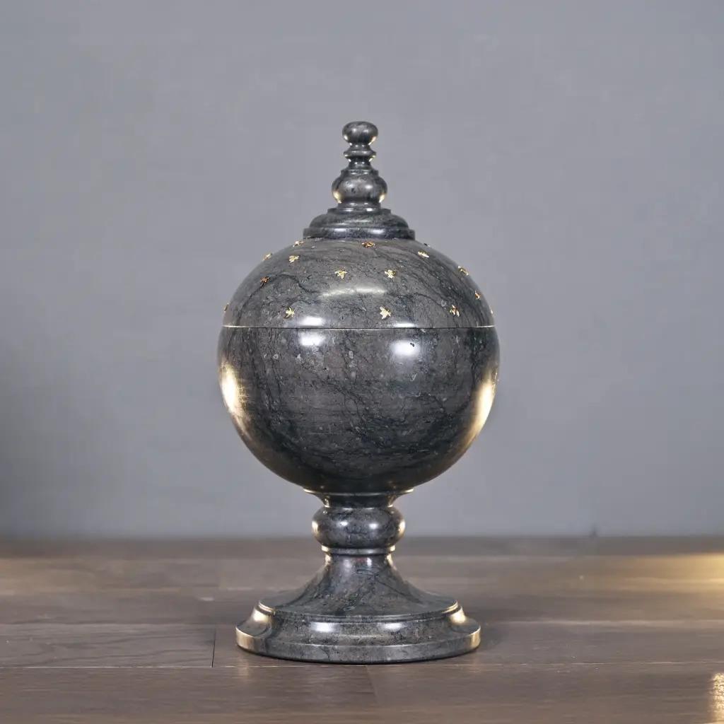 Questa elegante urna in marmo grigio/nero si ispira agli am designs classici del XIX secolo. È ornato da piccoli motivi di api dorate, popolari durante il periodo dell'Impero, che simboleggiano l'immortalità e la regalità.
Ogni urna è intagliata a
