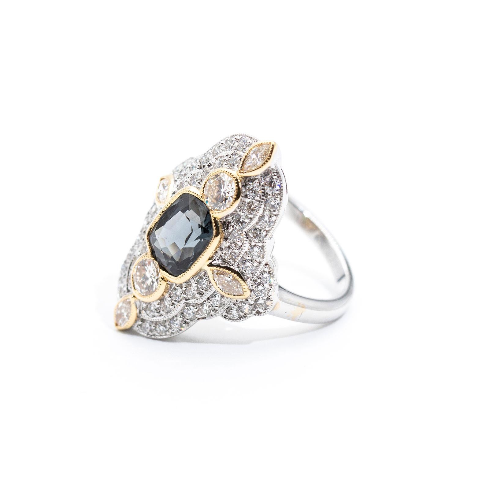 This striking vintage inspired cocktail ring is forged in 18 carat white and yellow gold and features a central beautiful bright 1.98 carat greyish blue natural cushion cut spinel. The spinel is surrounded by an alluring border of 1.54 carats of