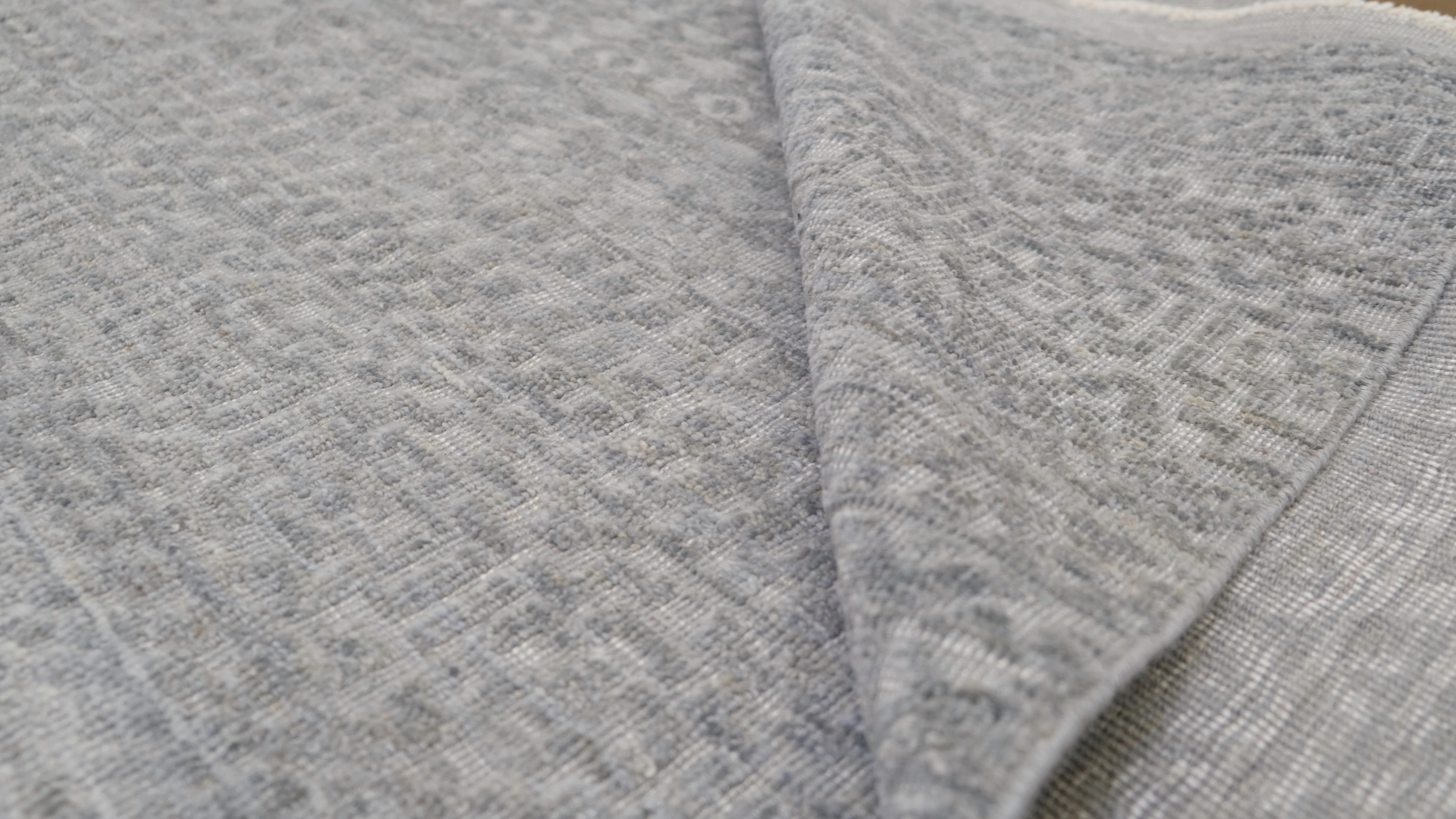 Bringen Sie schlichte Eleganz in Ihr Zuhause mit diesem handgeknüpften Wollteppich, der ein zartes und kompliziertes geometrisches Muster aufweist. Das raffinierte Design des Teppichs ist in sanften blauen Grautönen gehalten, wodurch eine zeitlose