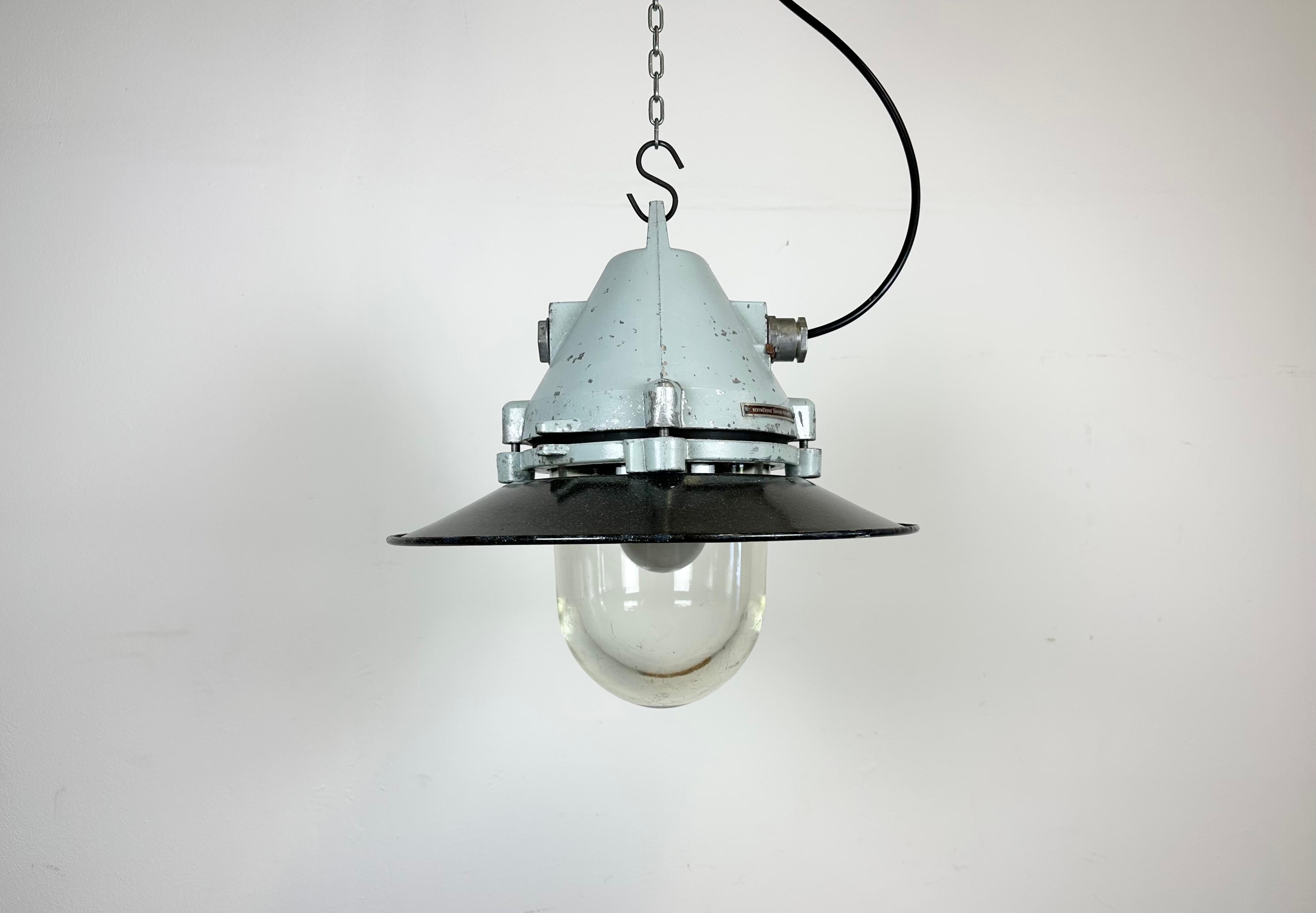 Grey industrial lamp with massive protective glass bulb made by Elektrosvit in former Czechoslovakia during the 1970s.It features a grey cast aluminium body, a clear glass and a grey enameled shade with white interior. Porcelain socket requires E27/