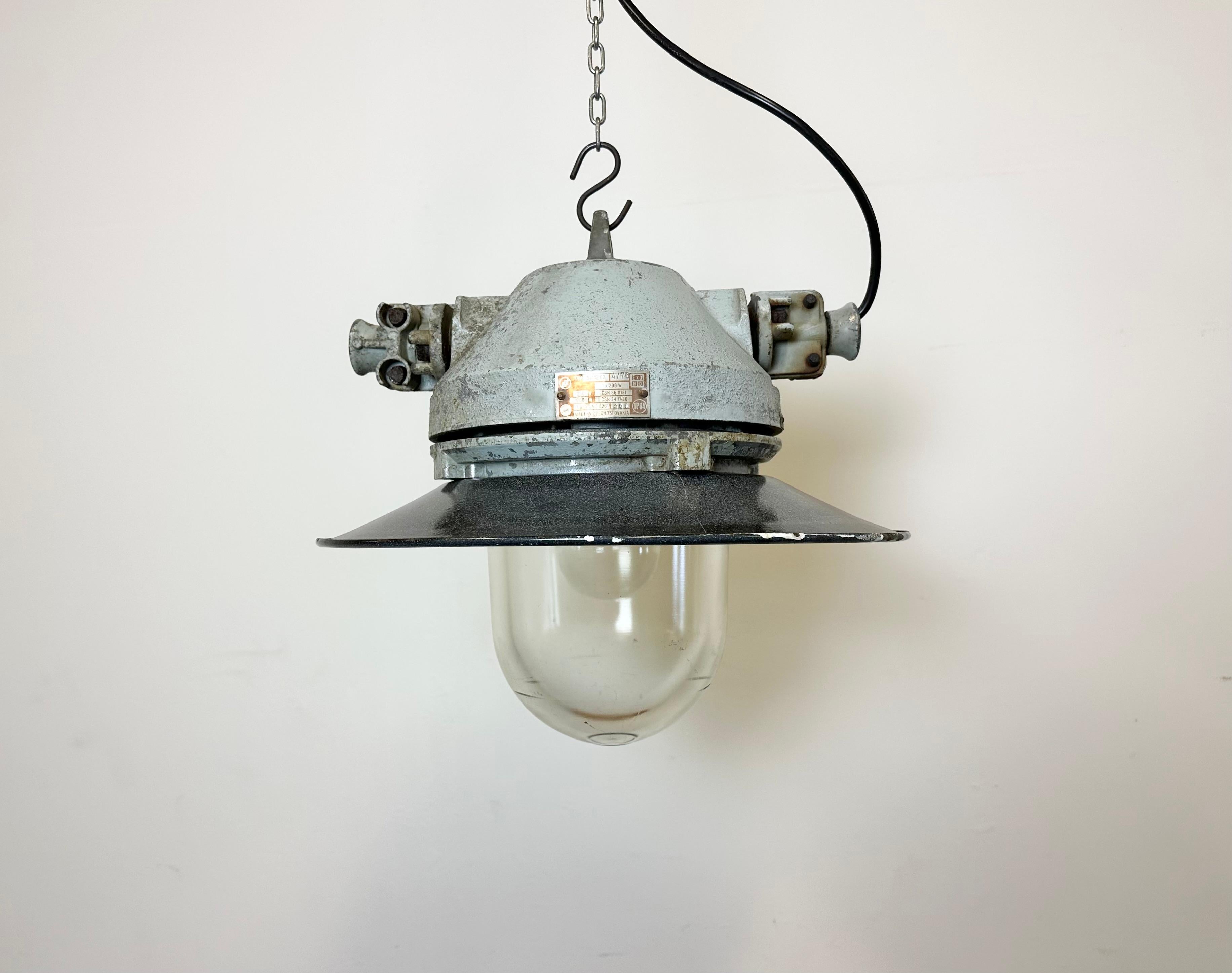 Grey industrial lamp with massive protective glass bulb made by Elektrosvit in former Czechoslovakia during the 1970s.It features a grey cast aluminium body, a clear glass and a grey enameled shade with white interior. Porcelain socket requires E27/