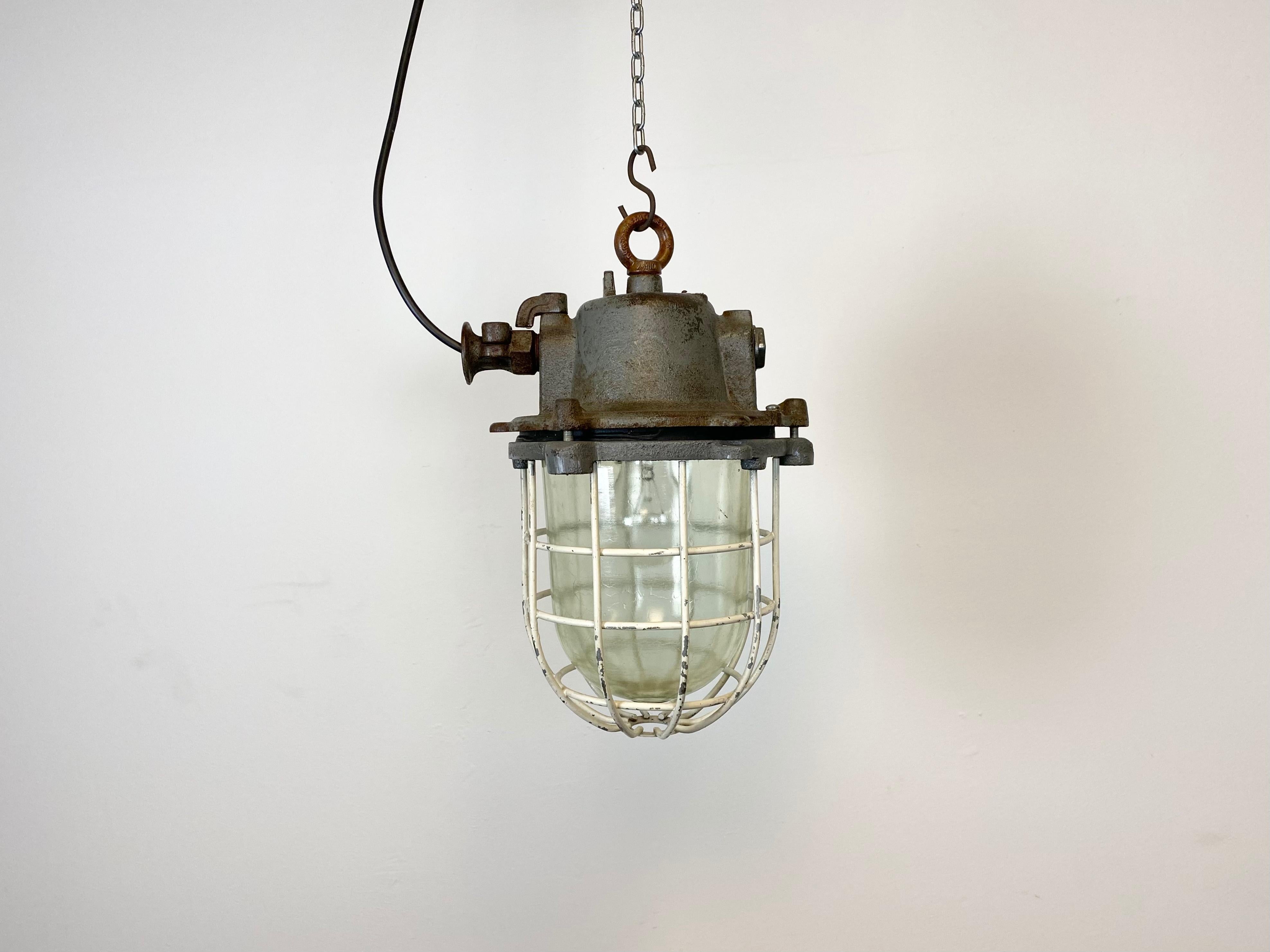 Industrial hanging lamp made by Elektrosvit in former Czechoslovakia during the 1970s. It features cast iron top, clear glass cover and iron grid. Porcelain socket for E 27 lightbulbs and new wire. The weight of the lamp is 8 kg.