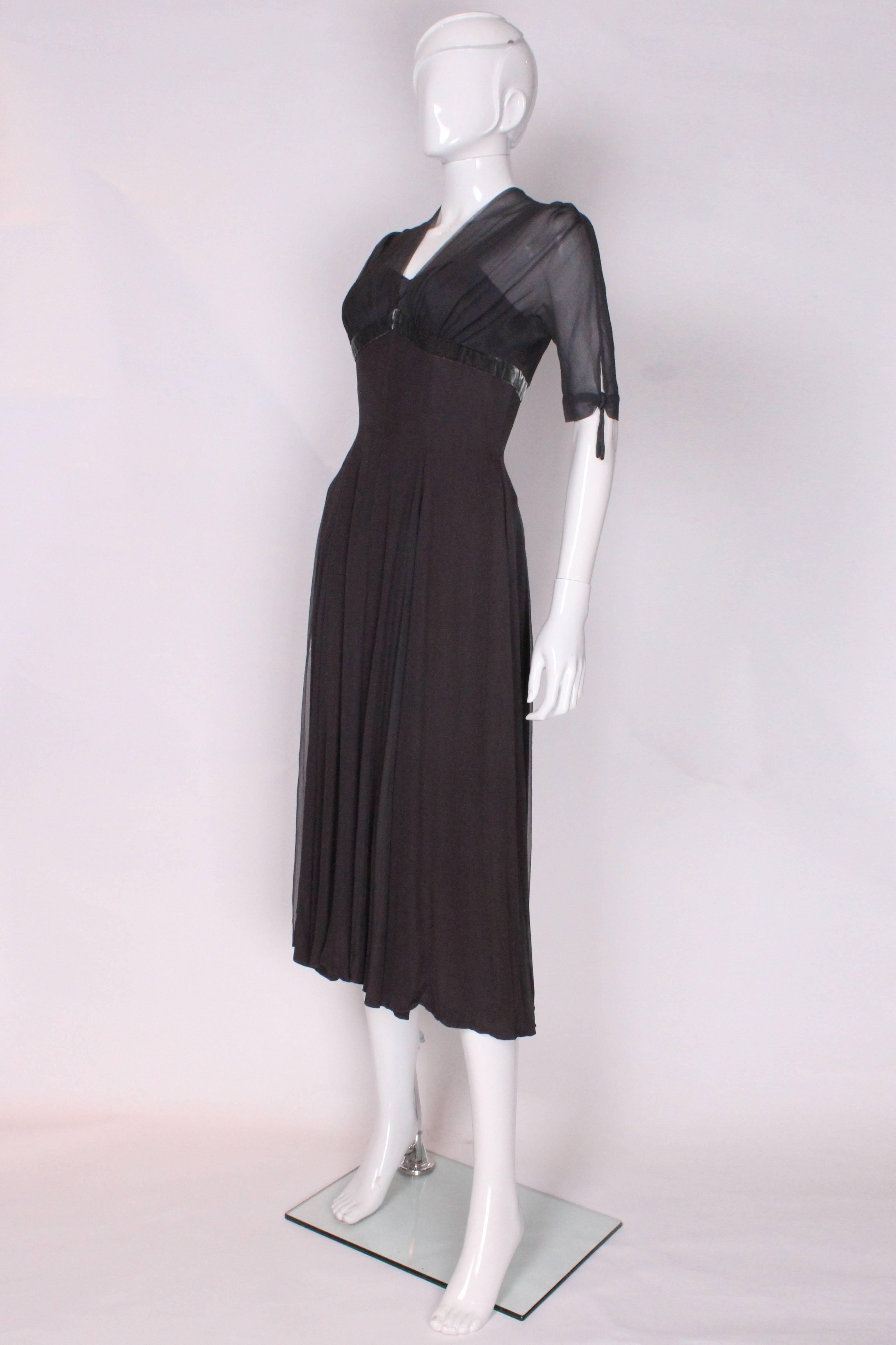 A chic cocktail dress designed by Worth, London. The dress has an outer layer of dark grey silk chiffon. The skirt is lined in a deep mauve/grey coloured fabric and the bust area in a slate grey. The dress has a v neckline and short sleeves. The
