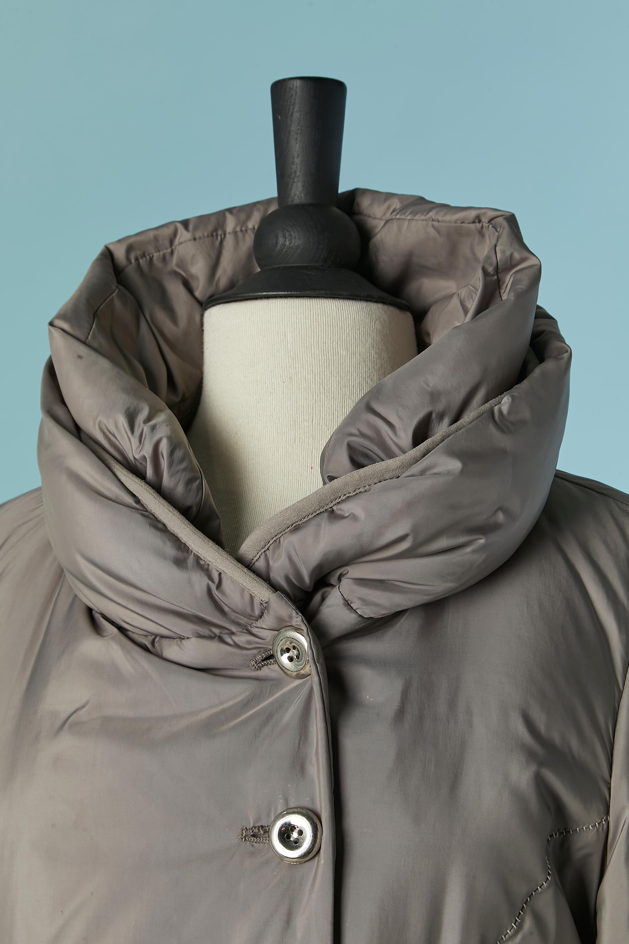 Piumino doppiopetto grigio con cappuccio. Tessuto principale, fodera e composizione delle coste: 100% poliestere.
Composizione dell'imbottitura: 80% oca, 20% piuma.
Chiusura con bottoni e asole sul centro del davanti. 
TAGLIA L 