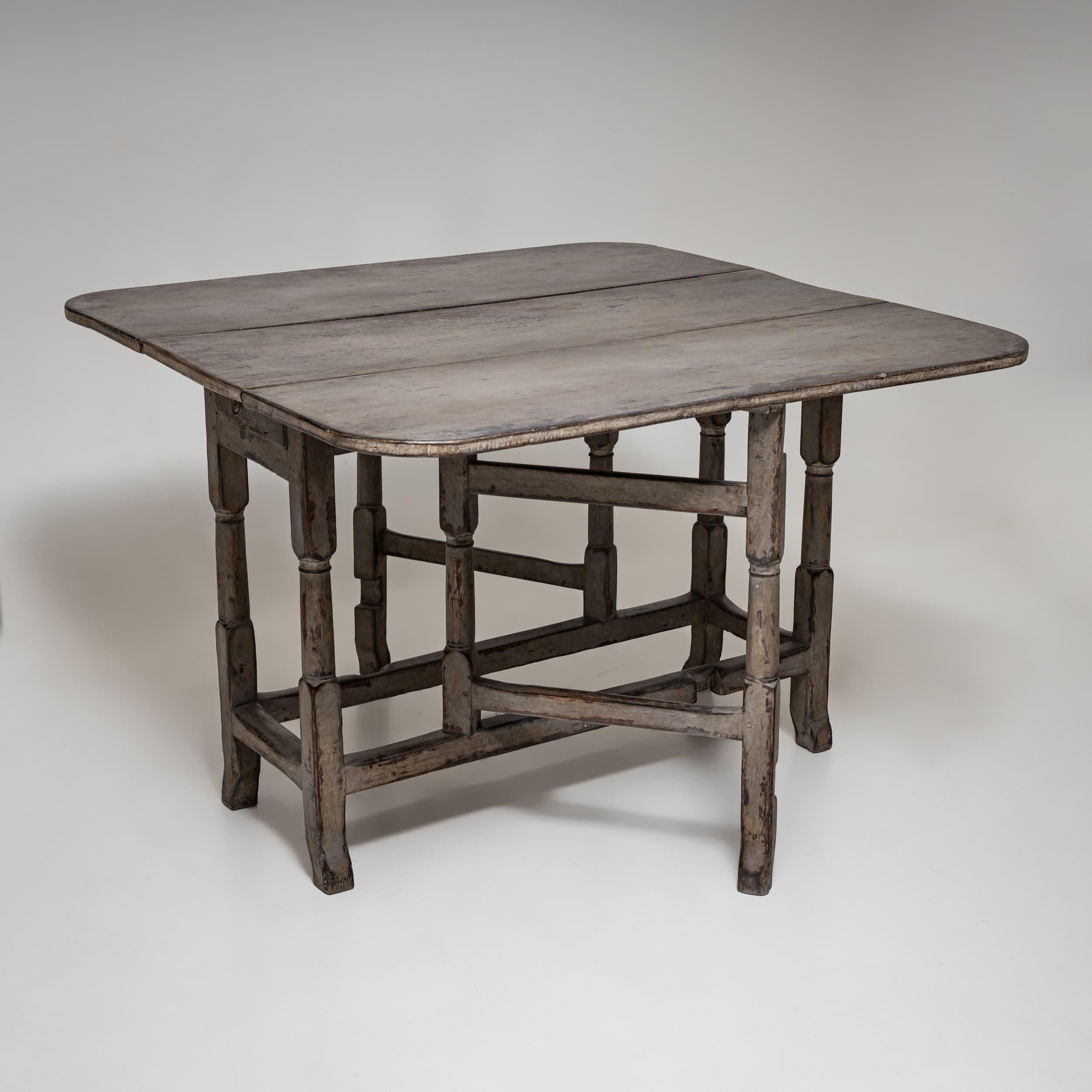 Eleganter Tortentisch mit hängenden Flügeln und gedrechselten Beinen, die durch stilvolle Streben verbunden sind. Die neu aufgetragene graue Oberfläche mit authentischer Patina unterstreicht den historischen Charme dieses vielseitigen Stücks. Mit