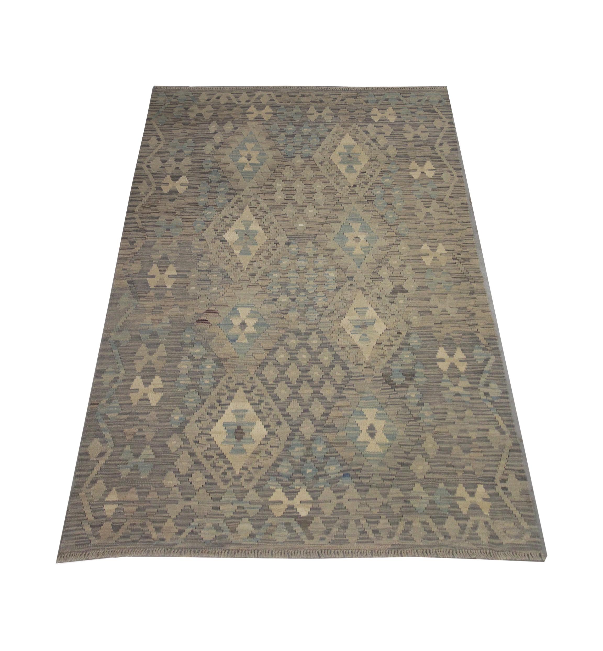 This fine wool area rug is a flatwoven Kilim woven by hand in the early 21st century in Afghanistan. The design features a bold geometric pattern woven with a subtle colour palette including grey, Light Brown, beige and blue. The varying subtle