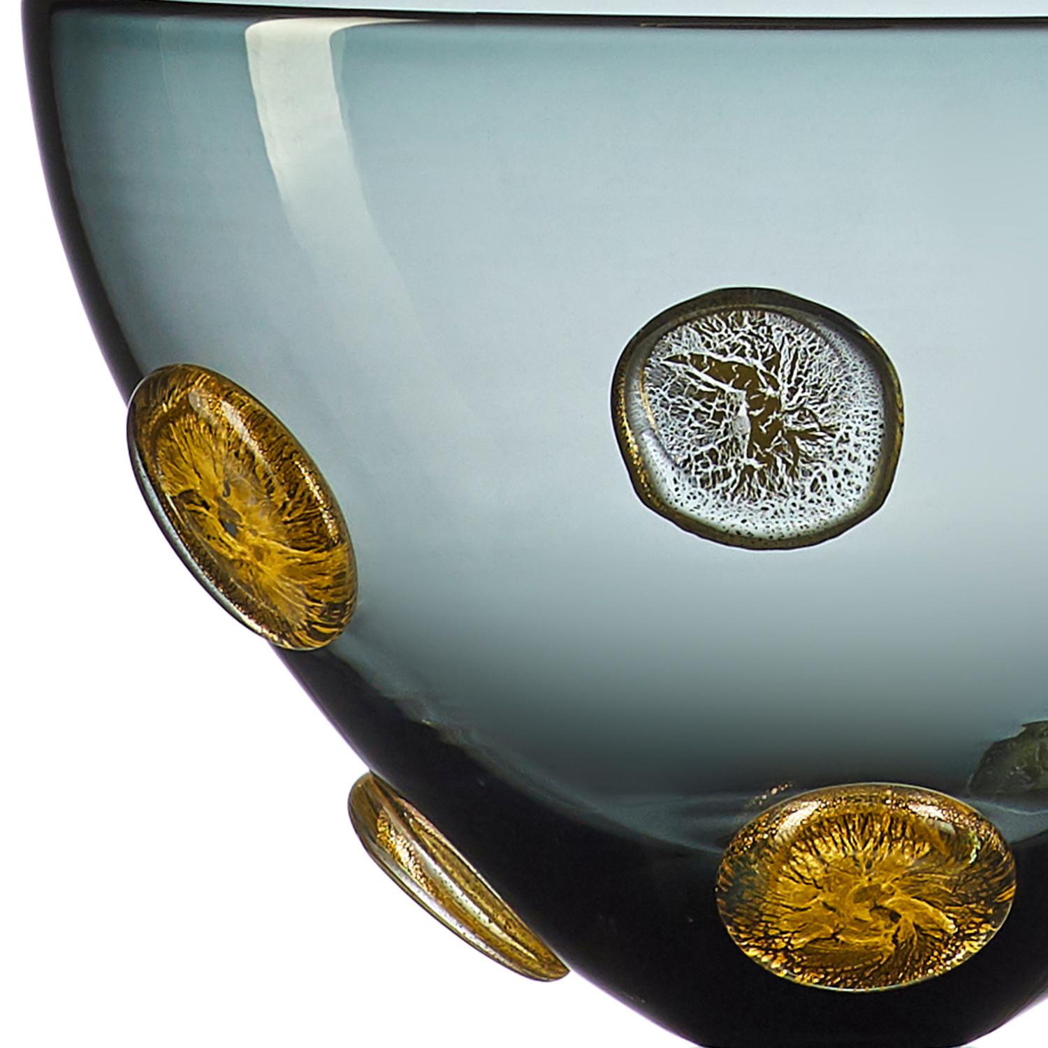 A luminous statement in translucent grey hand blown glass, the Moneto Bowl with Silver Dots features a Cascade of raised metallic coin-shaped dots, encased in clear glass. This large-scale designer vase is hand blown from start to finish by Vetro