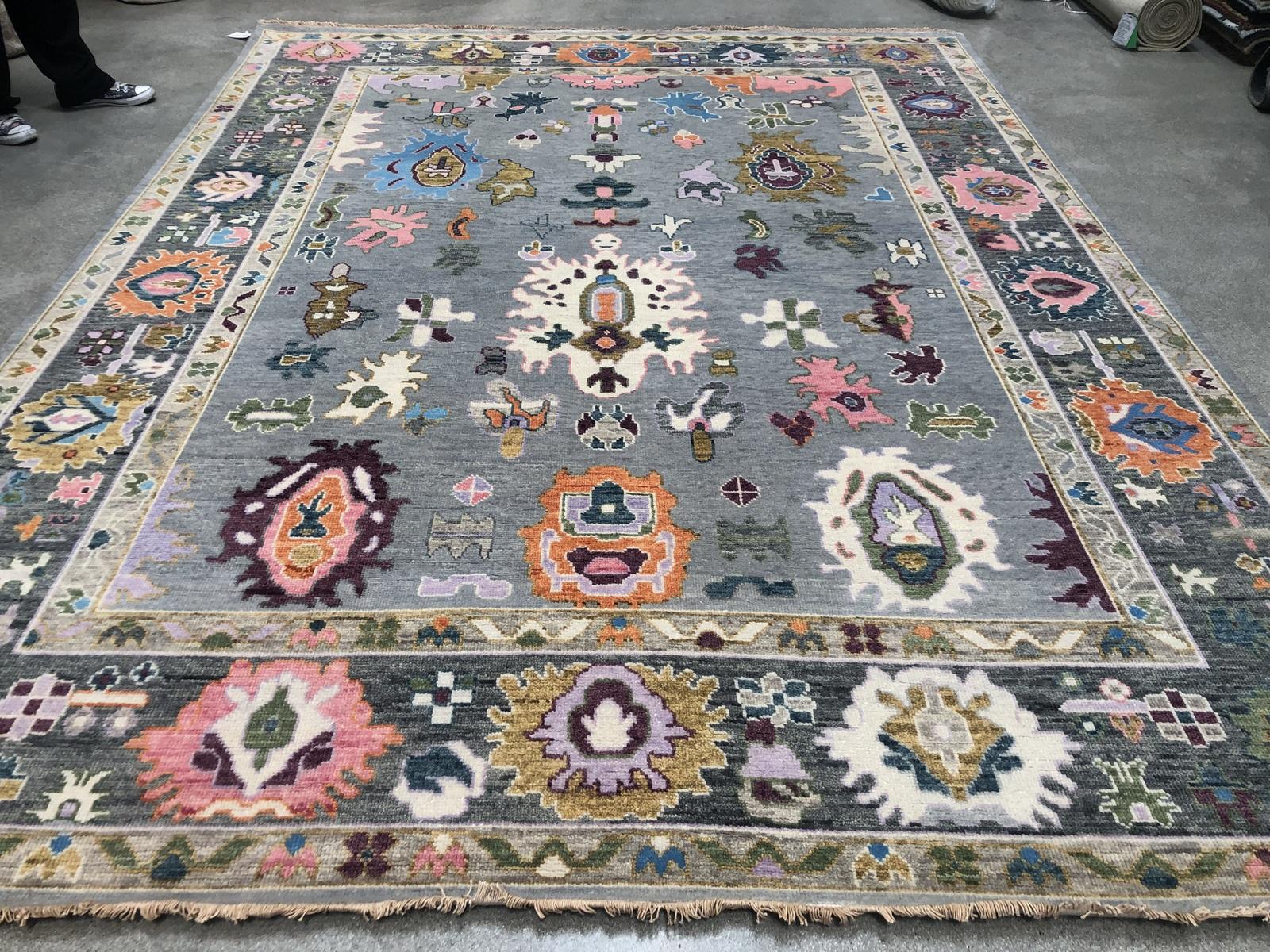 Whimsical abstract figures give this Indian wool area rug a decidedly tribal feel. The light grey center panel and dark grey border make the pink, orange, blue, ivory colors pop. A great piece to inject color into a space or round out a multi-color