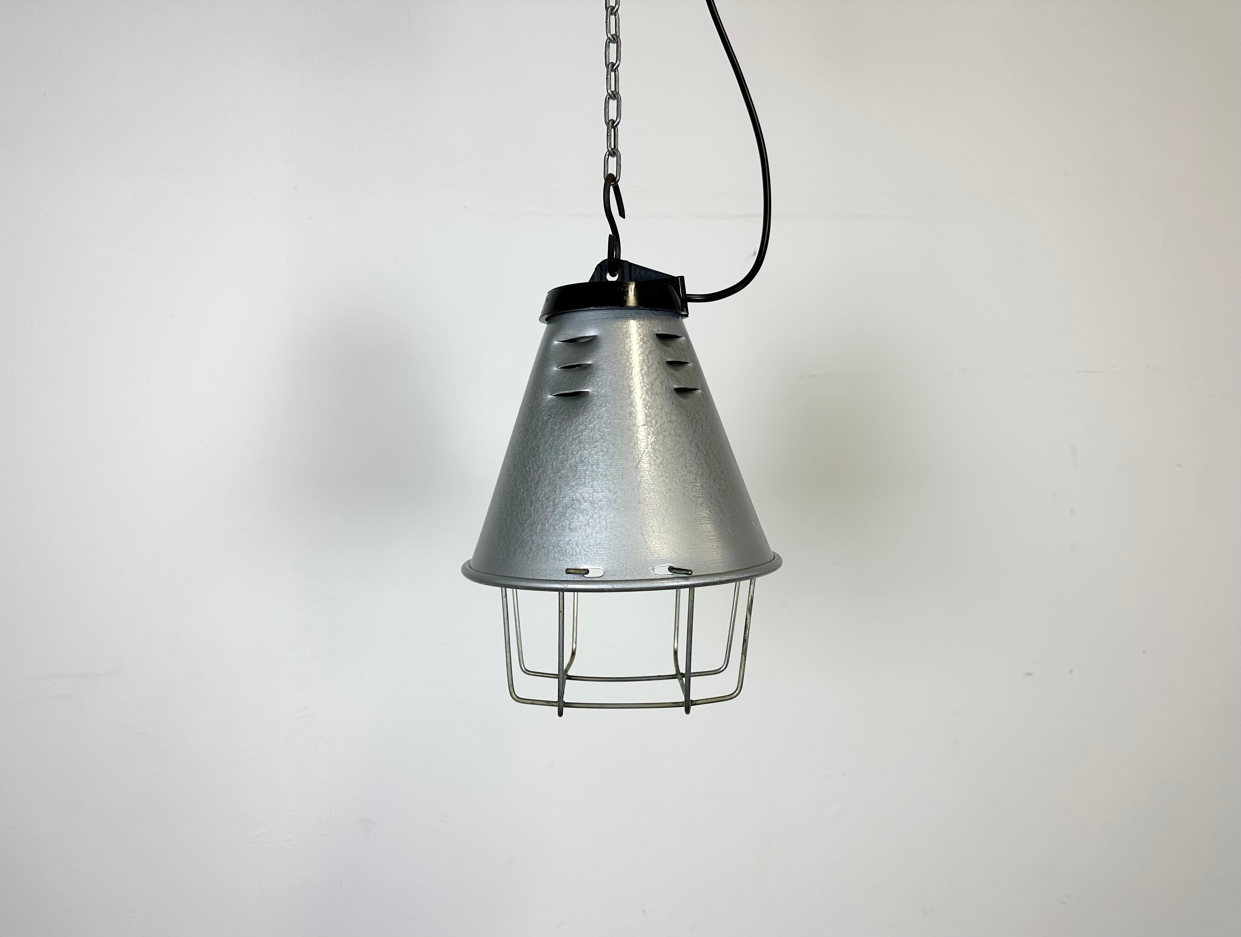 Industrial factory hanging lamp made by Polam Wilkasy in Poland during the 1970s. It features a grey hammerpaint aluminium shade, a black bakelite top and an iron grid. The original porcelain socket requires standard E 27/ E 26 lightbulbs. New wire.