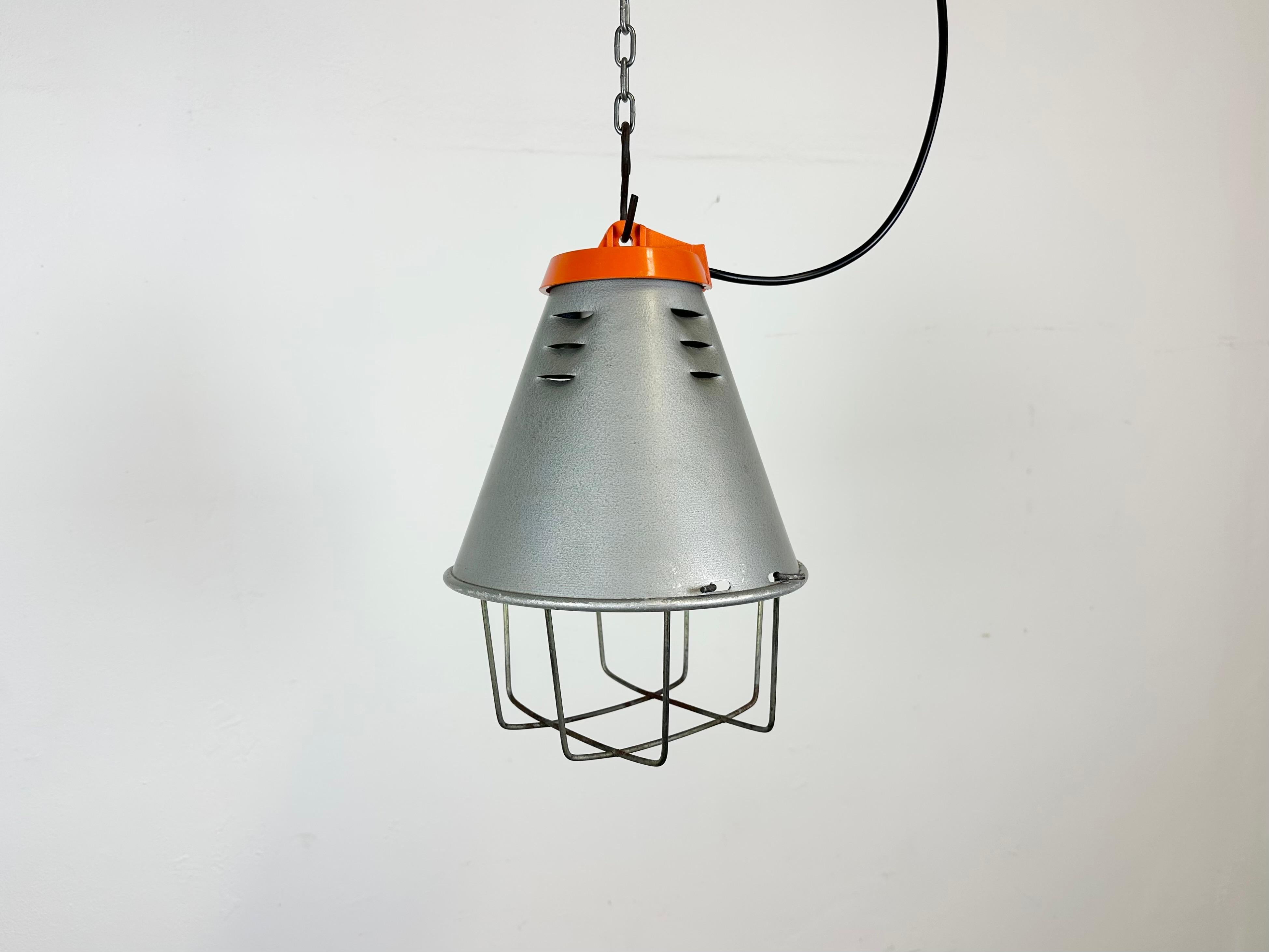 Industrial factory hanging lamp made by Polam Wilkasy in Poland during the 1970s. It features a grey hammerpaint aluminium shade, an orange bakelite top and an iron grid. The original porcelain socket requires standard E 27/ E 26 lightbulbs. New