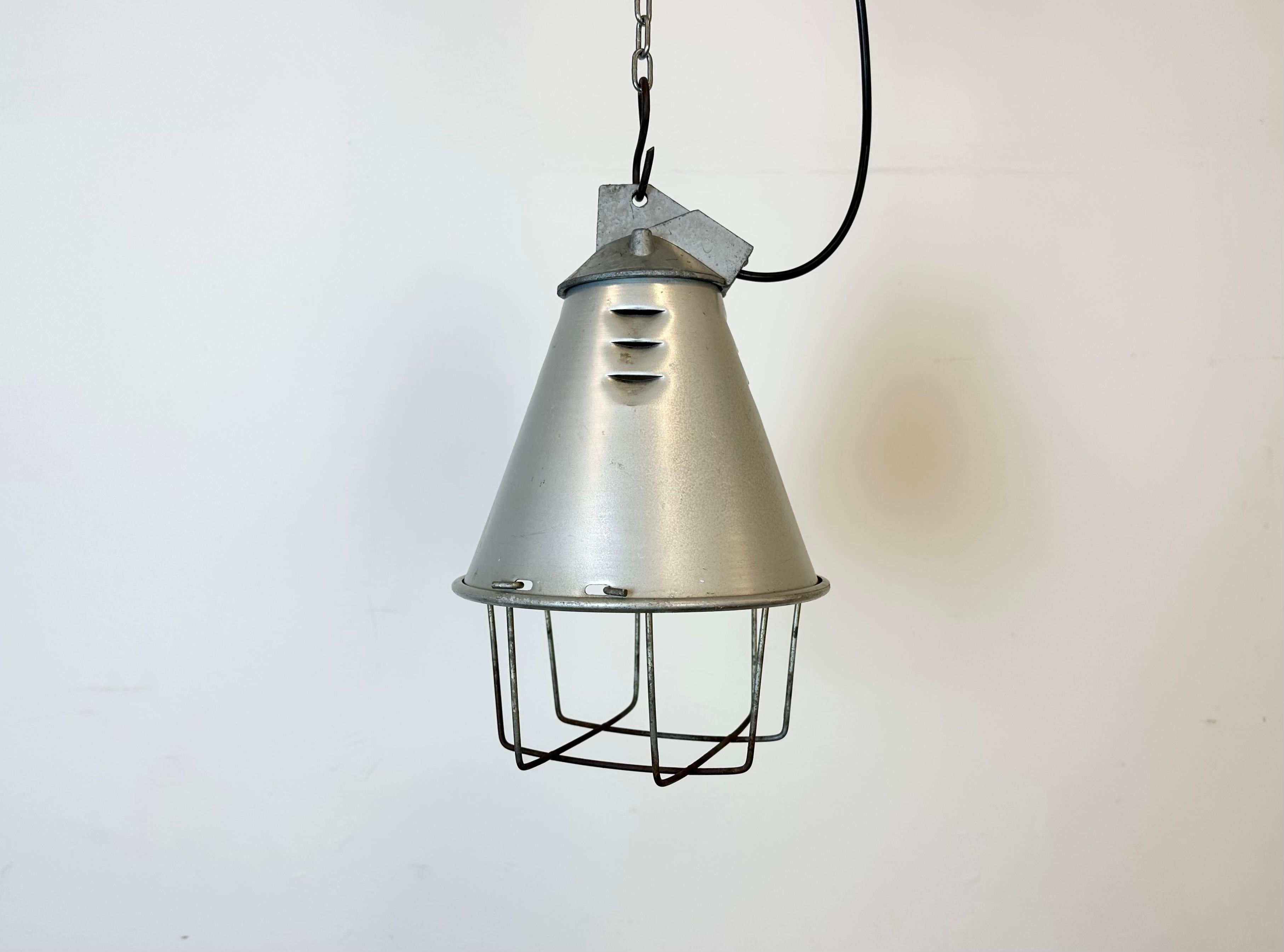 Industrial factory hanging lamp made by Polam Wilkasy in Poland during the 1970s. It features a grey aluminium shade, a cast aluminium top and an iron grid. The  porcelain socket requires standard E 27/ E 26 lightbulbs. New wire. The weight of the