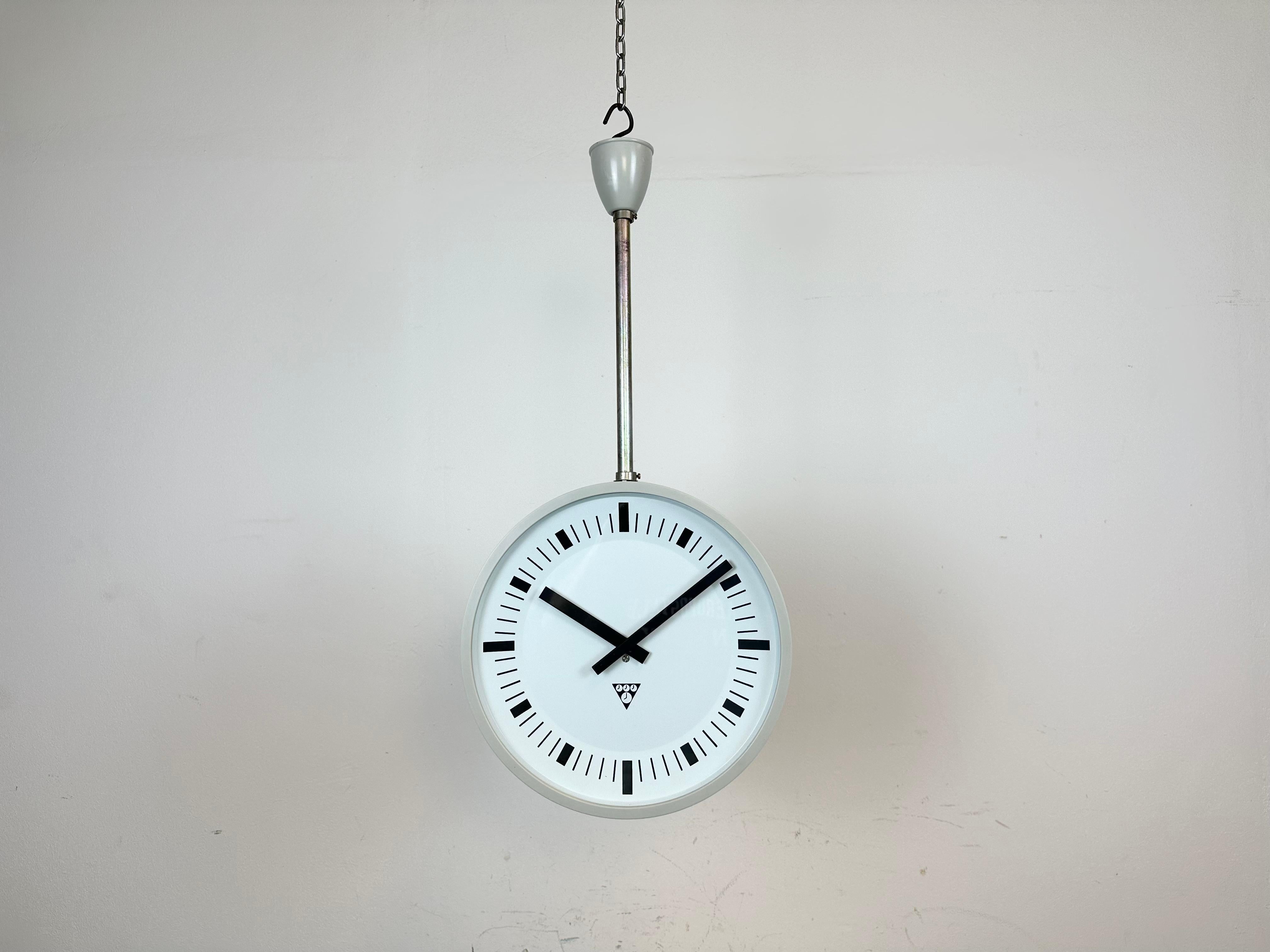 This factory or station double-sided factory clock was produced by Pragotron, in former Czechoslovakia, during the 1980s. The piece features a two grey bakelite clock with glass cover and iron ceiling mounting. Former slave clock has been converted