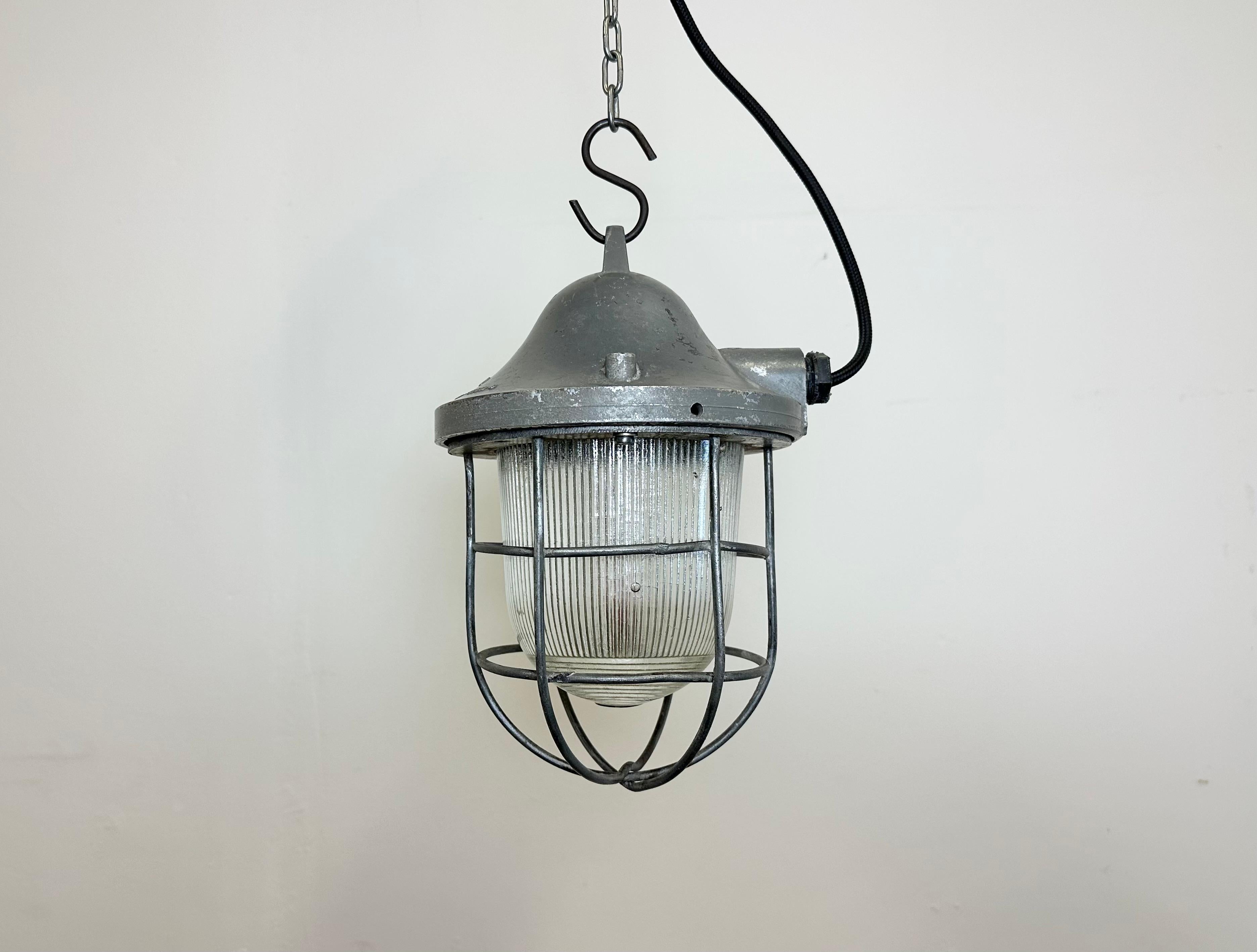 Grey industrial lamp made by Polam Gdansk in Poland during the 1960s. It features a cast aluminium body, an iron cage and striped glass. The porcelain socket requires standard E 27/ E 26 lightbulbs. New wire. The weight of the lamp is 1,8 kg.